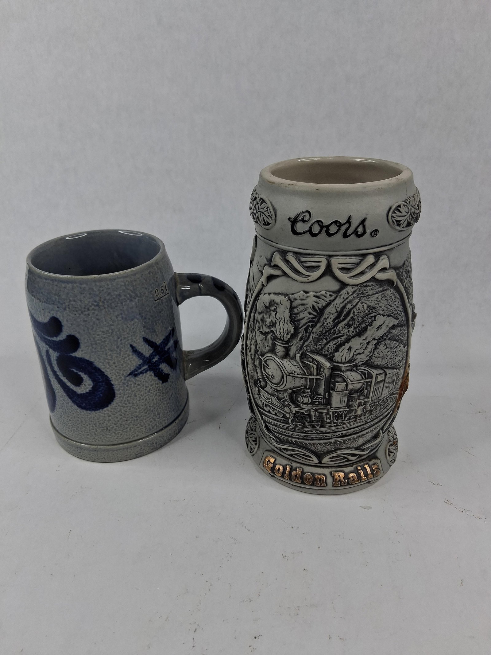 Coors & Marzi & Remy Stoneware Steins: This lot consists of two ceramic beer vessels: a traditional salt-glazed stoneware mug and a contemporary commemorative collector stein. The first item is a German stoneware mug produced by Marzi and 