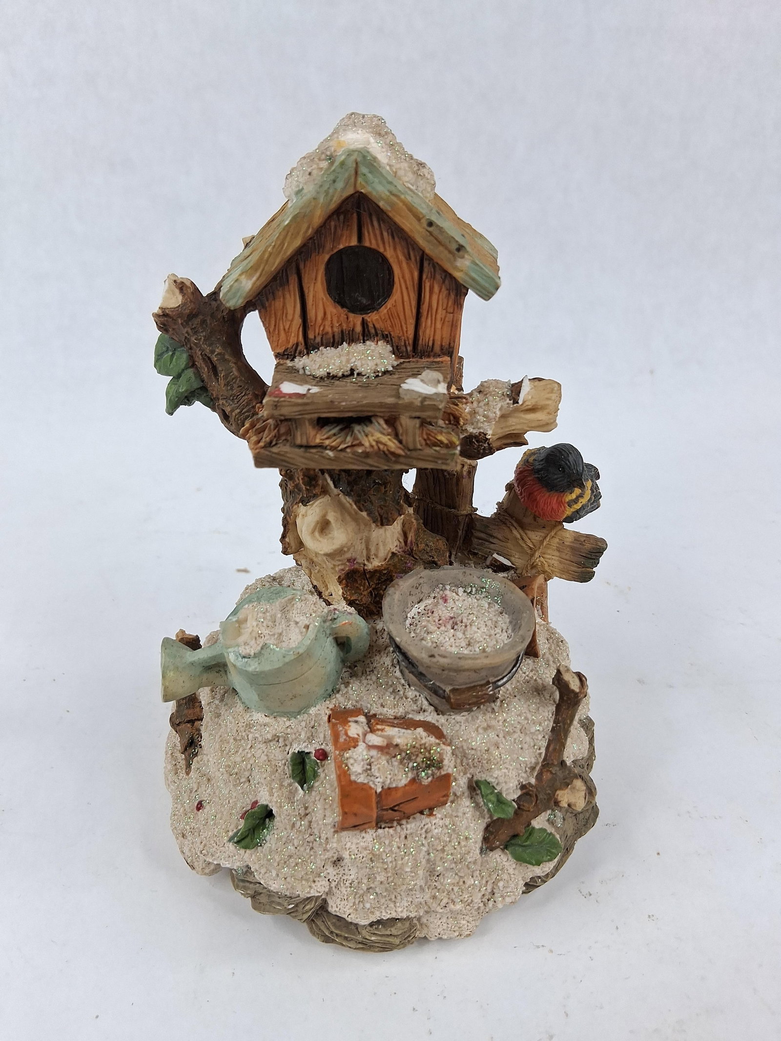 Sankyo Winter Birdhouse Music Figurine: A winter-themed musical figurine constructed of painted cast polyresin. The scene depicts a rustic wooden birdhouse mounted upon a snow-covered tree stump. Decorative elements include a small bird wit