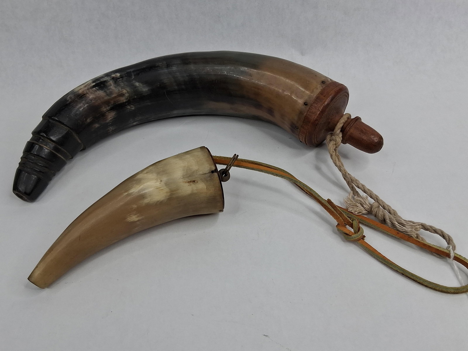 Two Black Powder Horns: Two traditional black powder horns of varying sizes, typically used for main charge and priming. The larger horn features a dark, polished tip with several turned concentric rings at the spout,