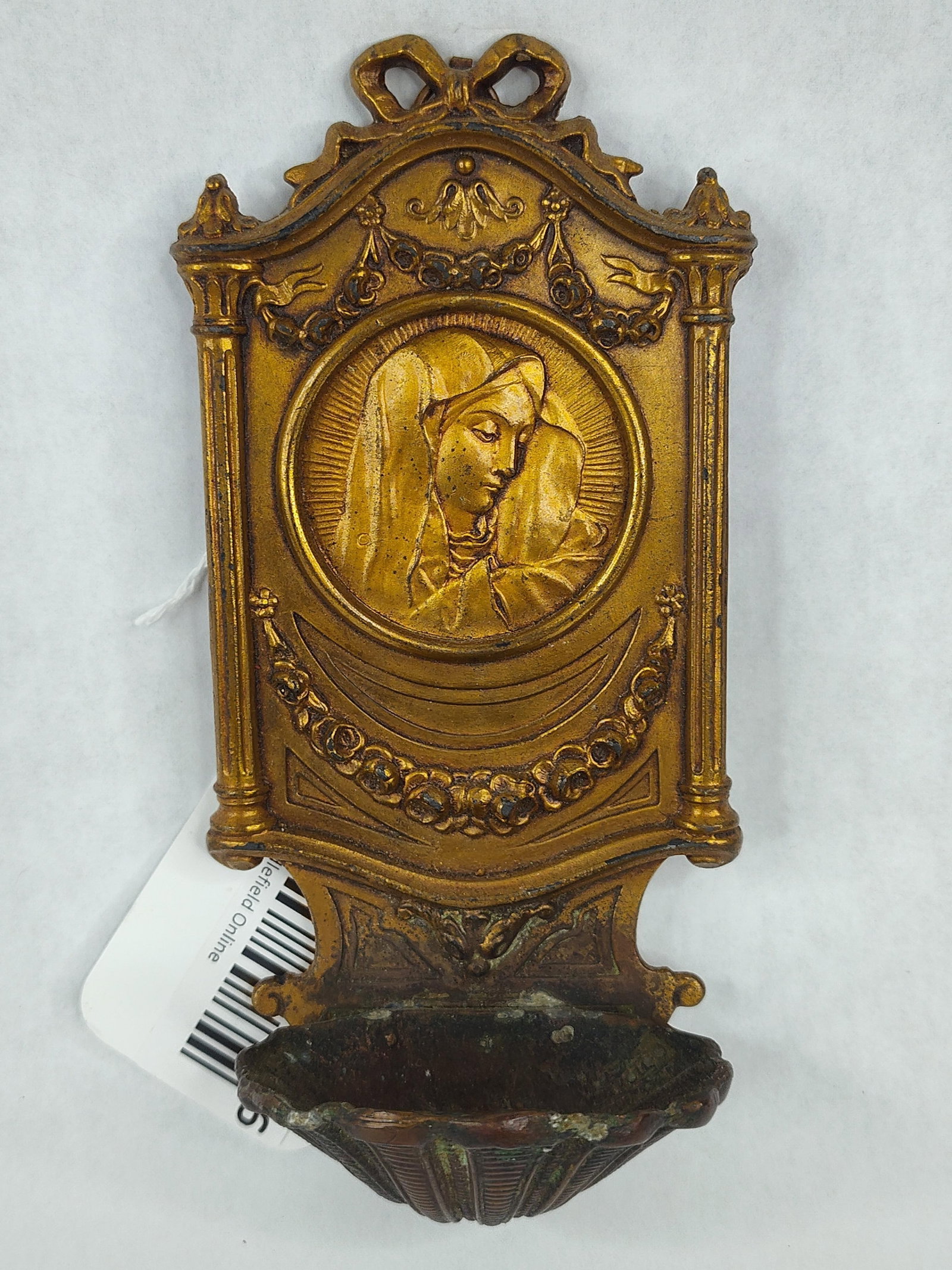 Jennings Bros Gilt Madonna Relief Font: A wall-hanging devotional holy water font constructed of gilded cast metal. The central feature is a circular relief medallion depicting the Virgin Mary in profile surrounded by a radiant halo. The or