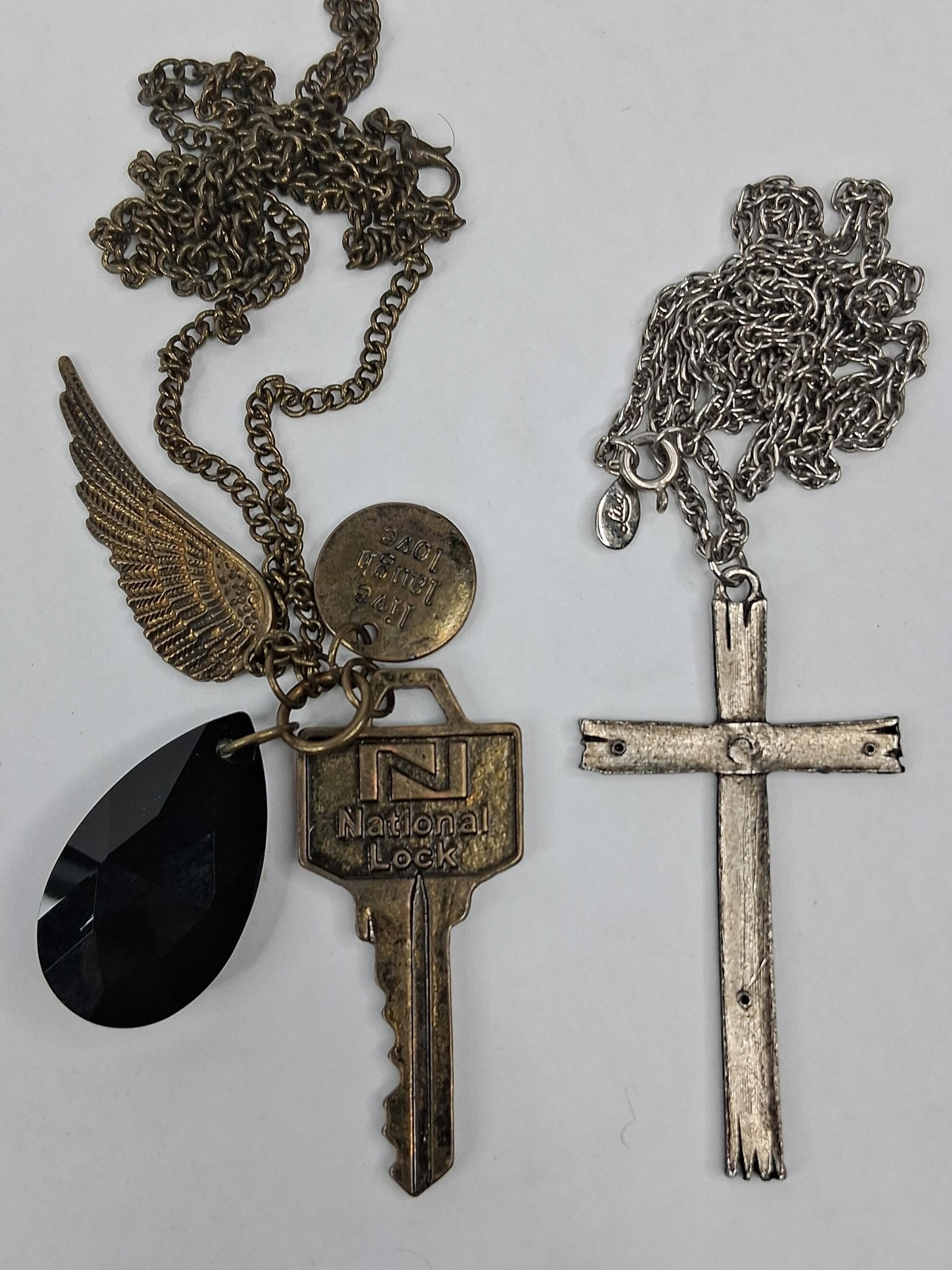 Lisa Cross & National Lock Key Pendants: This lot consists of two costume jewelry necklaces. The first is a multi-charm pendant necklace featuring a bronze-tone link chain and a lobster claw clasp. The charm assembly includes a large faceted