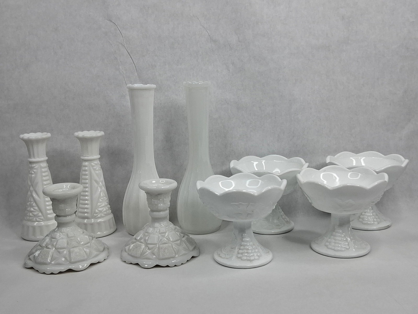 10 Vtg Harvest & Geometric Milk Glass: This collection consists of ten pieces of opaque white milk glass featuring a variety of embossed patterns and forms. The assortment includes a pair of tall, slender bud vases characterized by