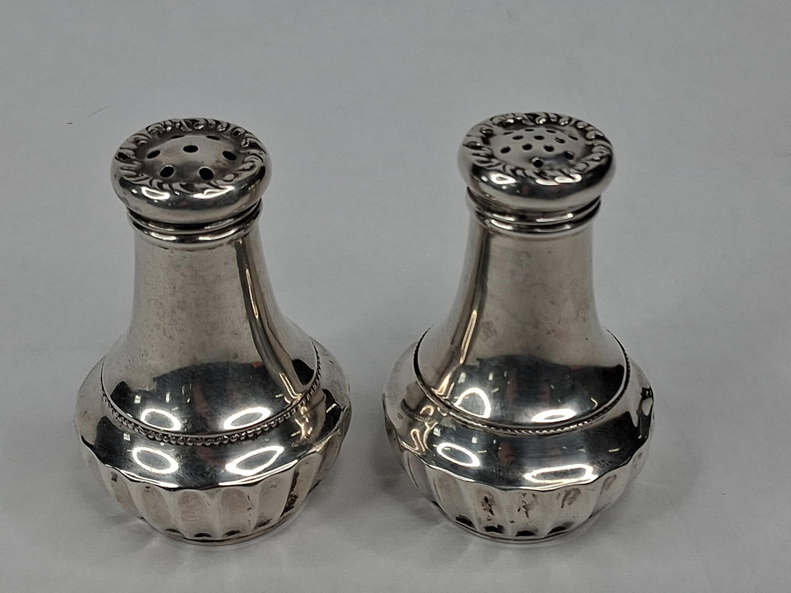 Pair Int'l Silver Str. S&P Shakers 020: A pair of sterling silver salt and pepper shakers produced by the International Silver Company. Each shaker is designed in a classical baluster form with a polished finish. The shoulder is accented