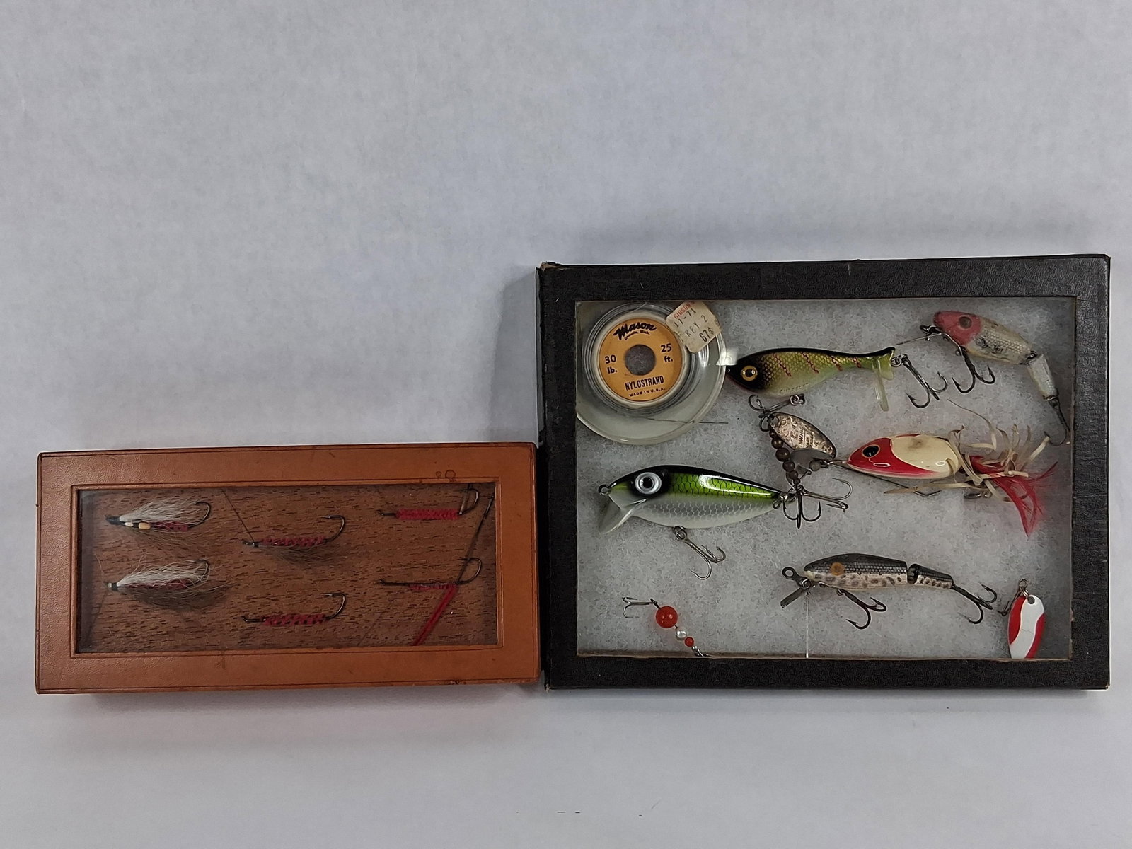 Heddon & Mason Vtg Lures & Tied Flies: A collection of fishing tackle presented in two display boxes. The first is a rectangular wooden box with a tan leatherette exterior and a glass viewing panel, containing several hand-tied fishing