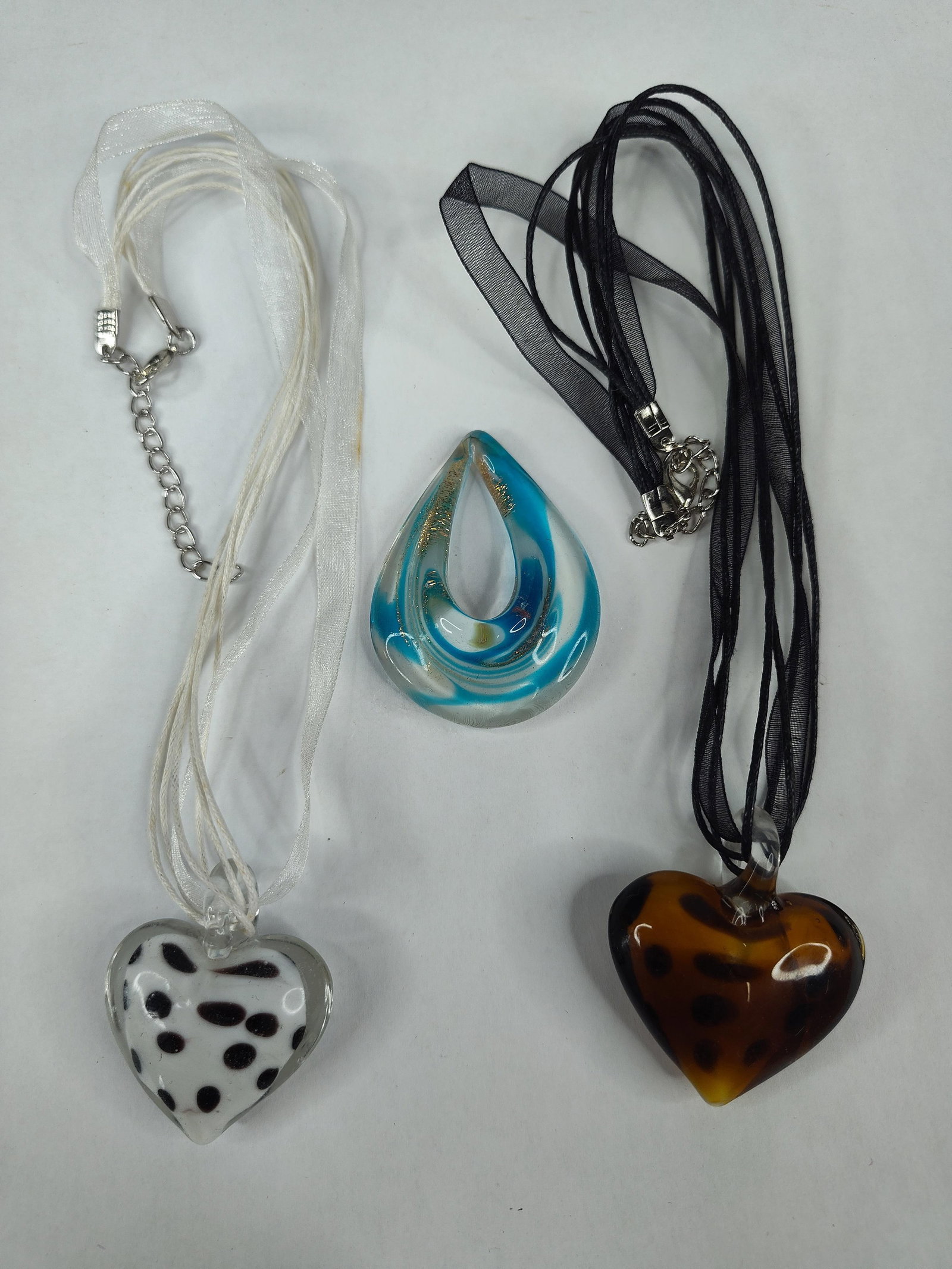Trio Art Glass Pendants & Necklaces: This lot consists of three contemporary art glass pendants, two of which are assembled as necklaces. The first necklace features a heart-shaped glass pendant with an opaque white core decorated with d
