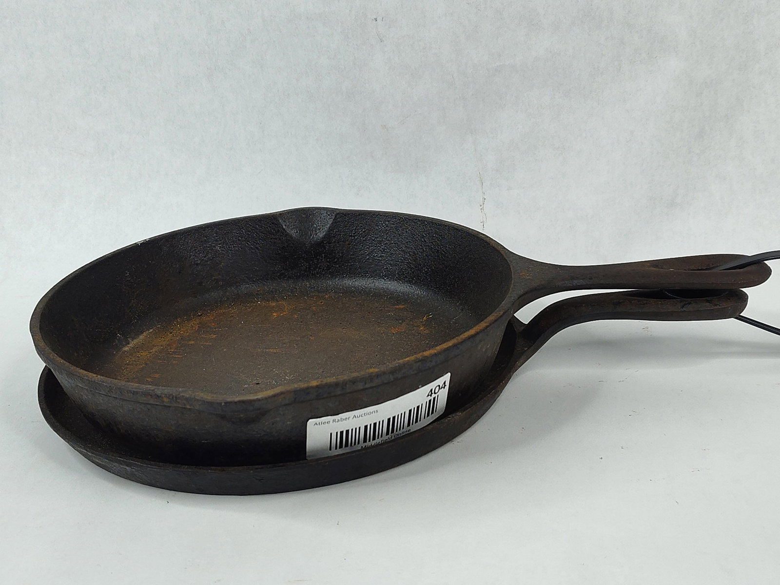 Pair Vtg Lodge Cast Iron Cookware: This lot features two American cast iron cookware items from the Lodge Manufacturing Company. Included is a number 8 skillet with dual pour spouts and a teardrop-shaped handle. The base of the skillet
