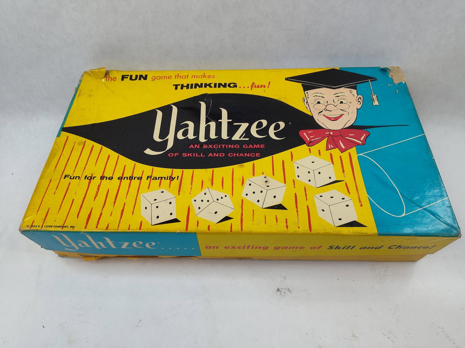 E. S. Lowe Company Yahtzee Game w/ Box: This Yahtzee dice game was manufactured by the E. S. Lowe Company, Inc. The set is constructed from cardboard, paper, plastic, and faux-leather materials. It includes the original illustrated cardboar
