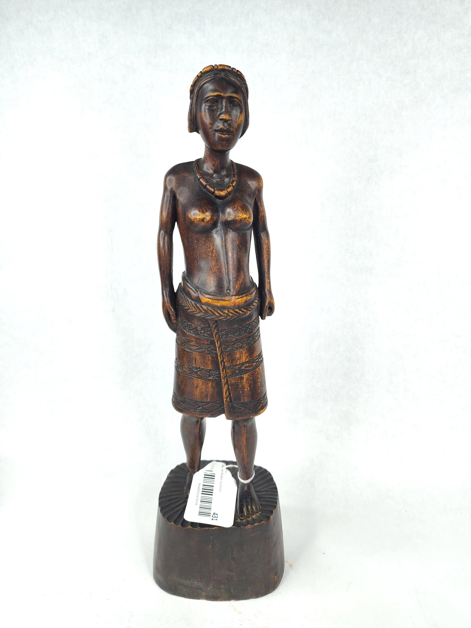 African Style Carved Wood Female Figure: A hand-carved wooden sculpture representing a standing female figure. The figure is depicted with a stylized headband or coiffure, a carved beaded necklace, and bare breasts. She wears a wrap-around