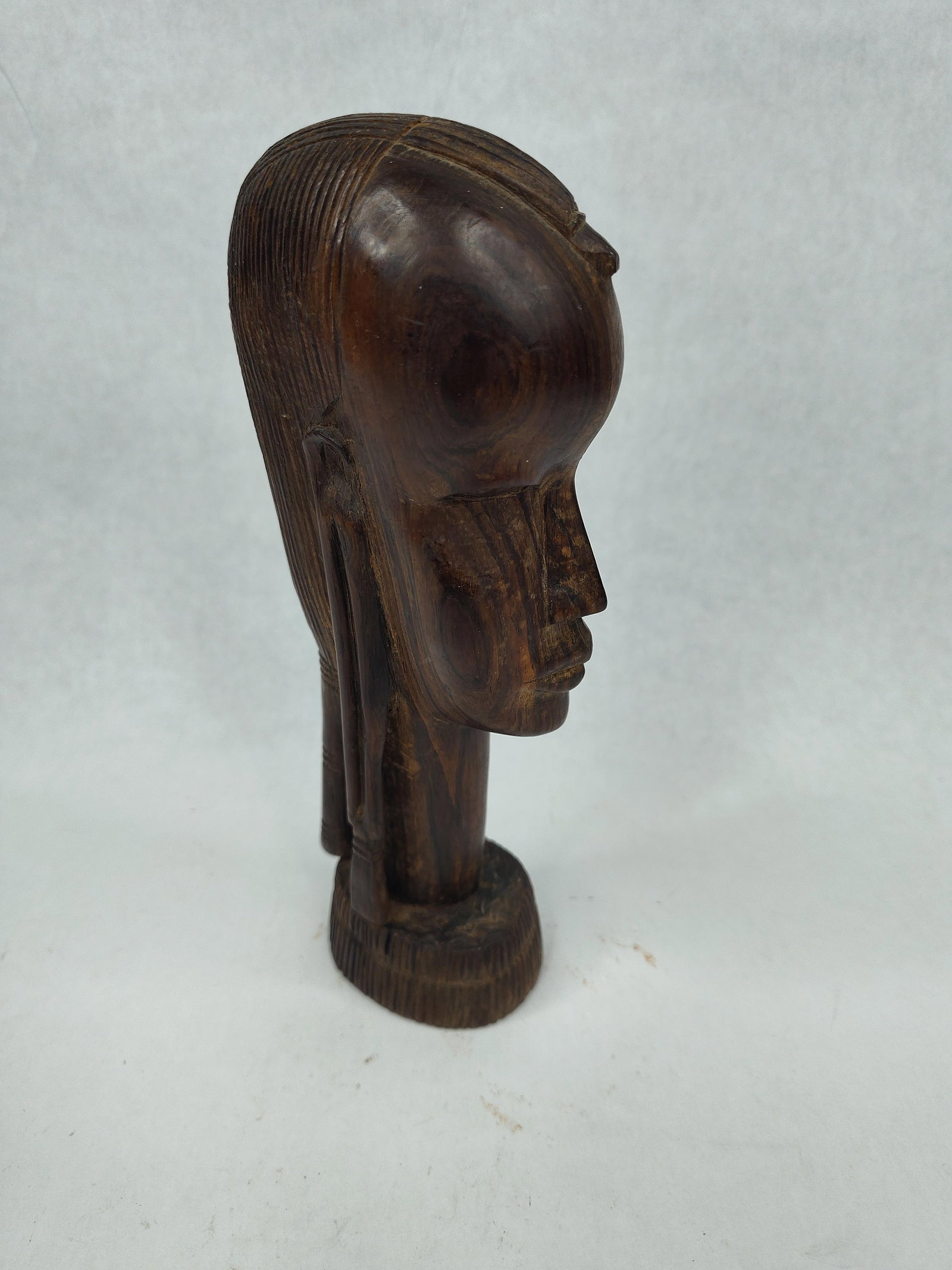 African Maasai Carved Ebony Wood Bust: A hand carved wooden bust sculpture depicting a stylized head in the Maasai tradition of East Africa. The piece is carved from a single block of solid ebony wood, exhibiting a dark brown heartwood and