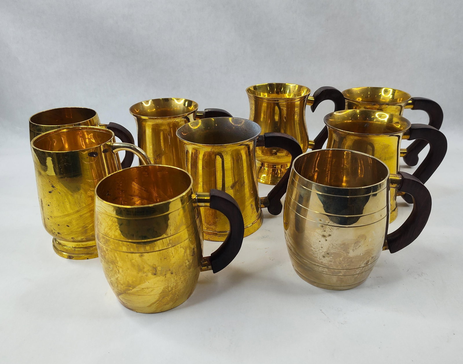 Set 10 TS Brass Mugs & Tankards w/ Wood: A group of ten brass drinking vessels manufactured by TS in India. This collection comprises ten pieces in three distinct styles: three barrel-shaped mugs with horizontal incised banding, five flared 