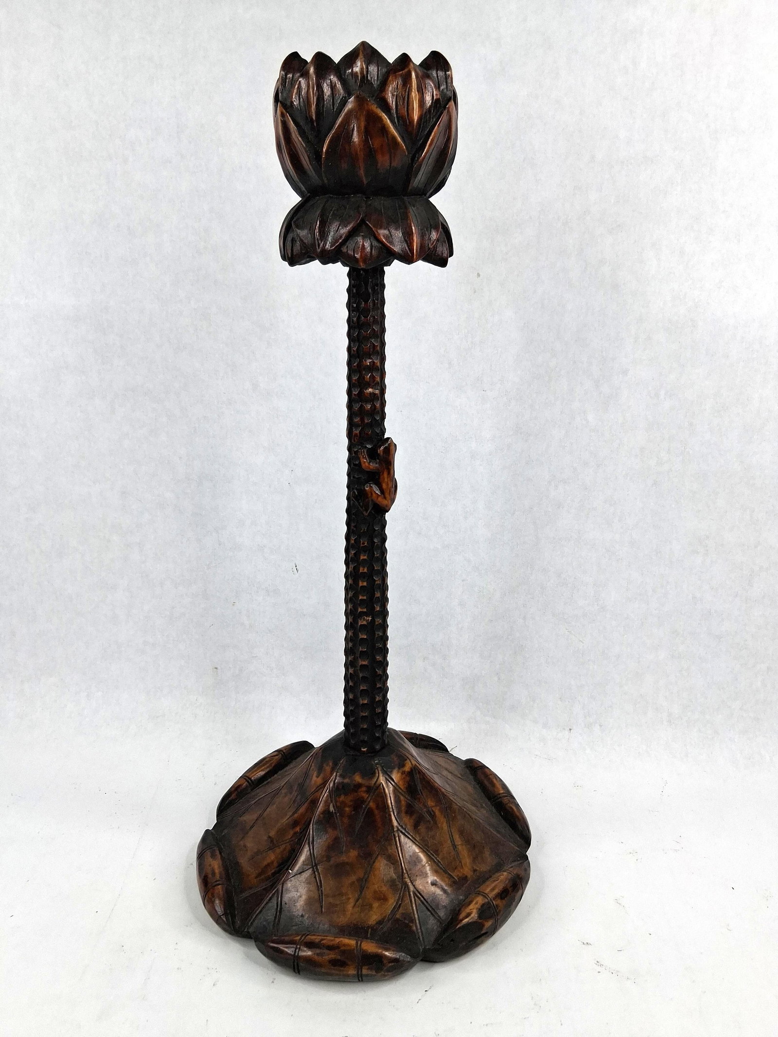 Carved Wood Lotus and Frog Candlestick: A hand-carved wooden candlestick featuring a naturalist motif. The piece consists of a candle cup in the form of a lotus blossom set atop a slender stem. The stem features a repeating pitted texture a