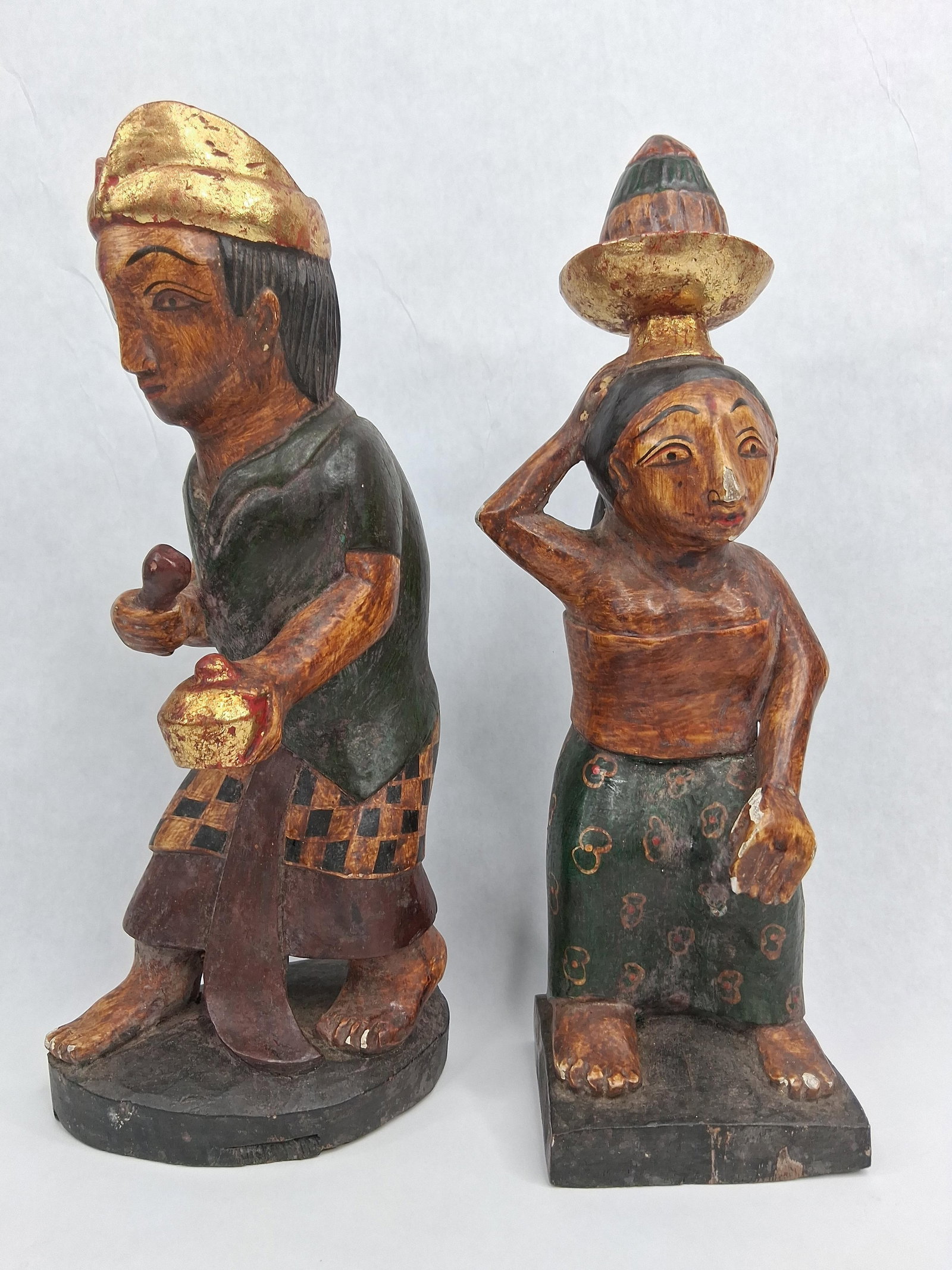 Pair Balinese Gilt & Polychrome Figures: A pair of hand-carved wooden figures from Bali, finished with polychrome paint and gilded accents over a gesso ground. One figure depicts a male in a dynamic, semi-crouched posture, wearing a gilded u