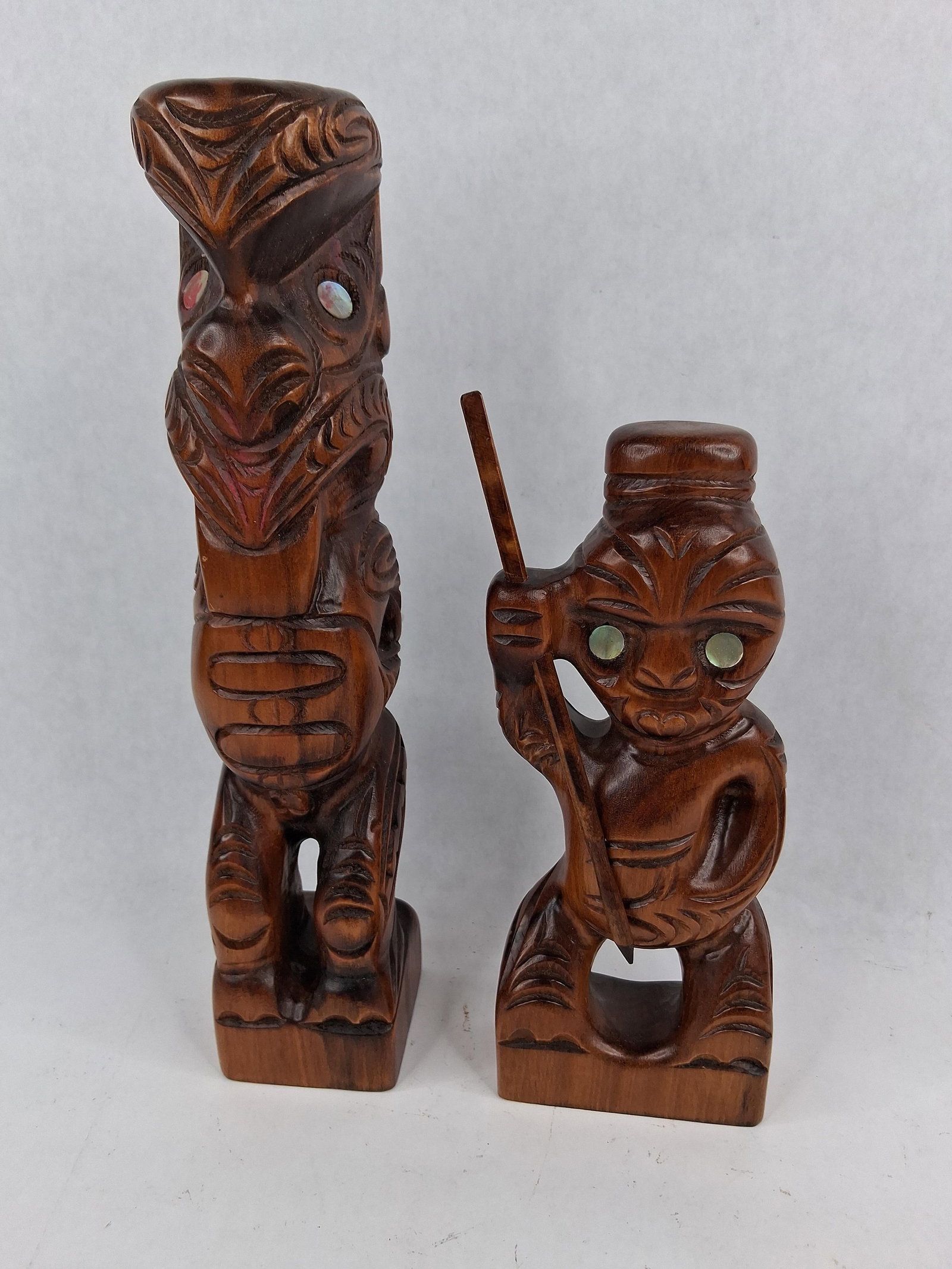 Pair Maori Wood Figurines w/ Paua Shell: Two traditional Maori-style figurines hand-carved from dark-stained wood, characteristic of indigenous art forms from Aotearoa (New Zealand). The lot consists of a taller stylized figure and a