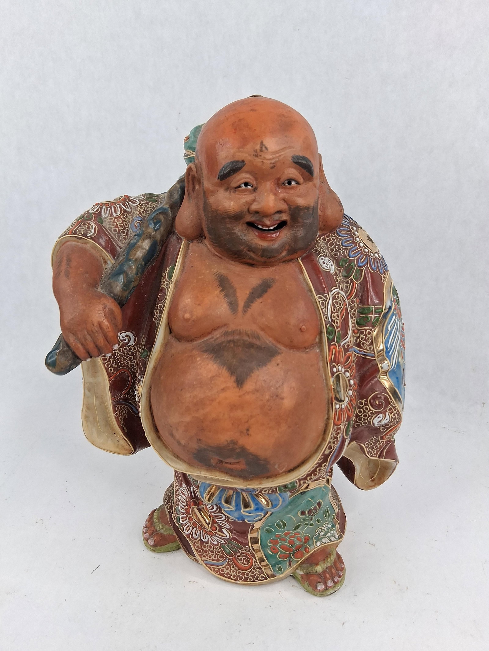 Kutani Moriage Porcelain Hotei Figure: A Japanese polychrome ceramic figure of Hotei, the God of Contentment and one of the Seven Lucky Gods. The figure is decorated in the Kutani style featuring heavy moriage raised enamel work and extens
