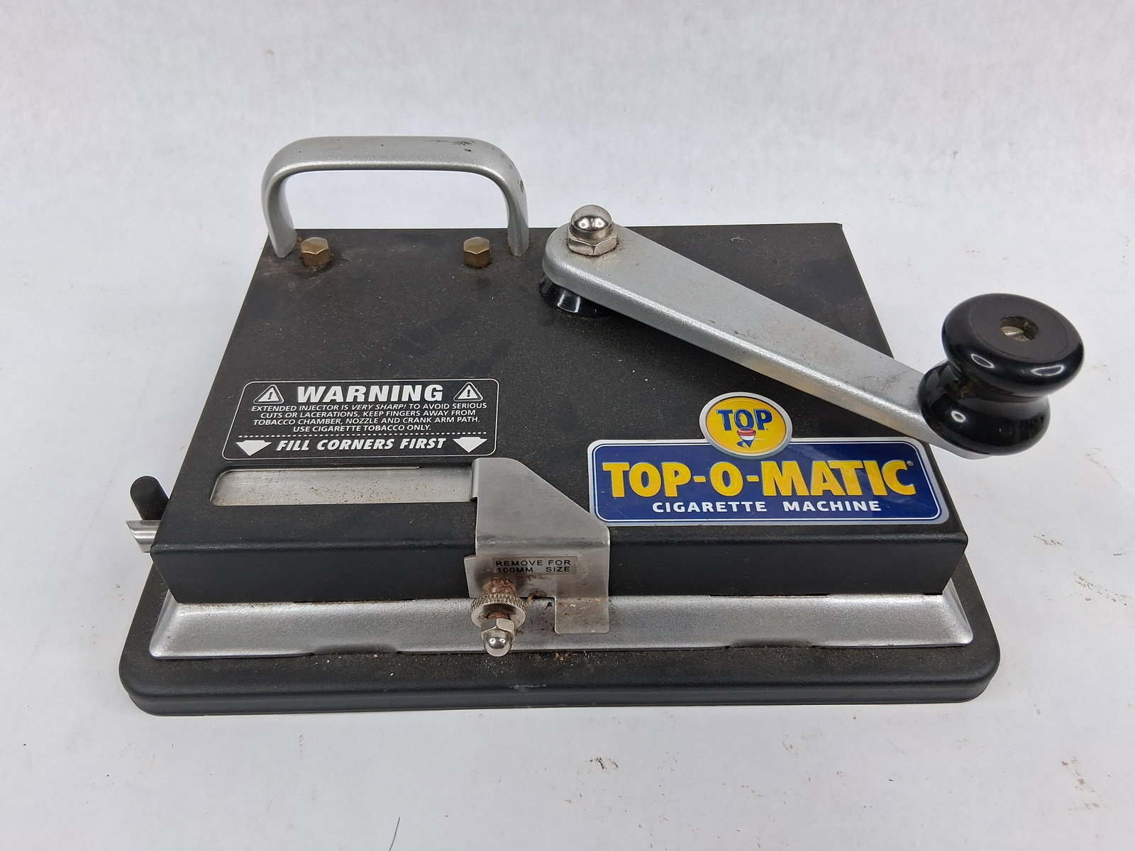 Top-O-Matic Manual Cigarette Injector: A Top-O-Matic manual desktop cigarette injector machine featuring a black-coated metal body with a silver-toned crank arm and carrying handle. This mechanical device is designed to inject tobacco