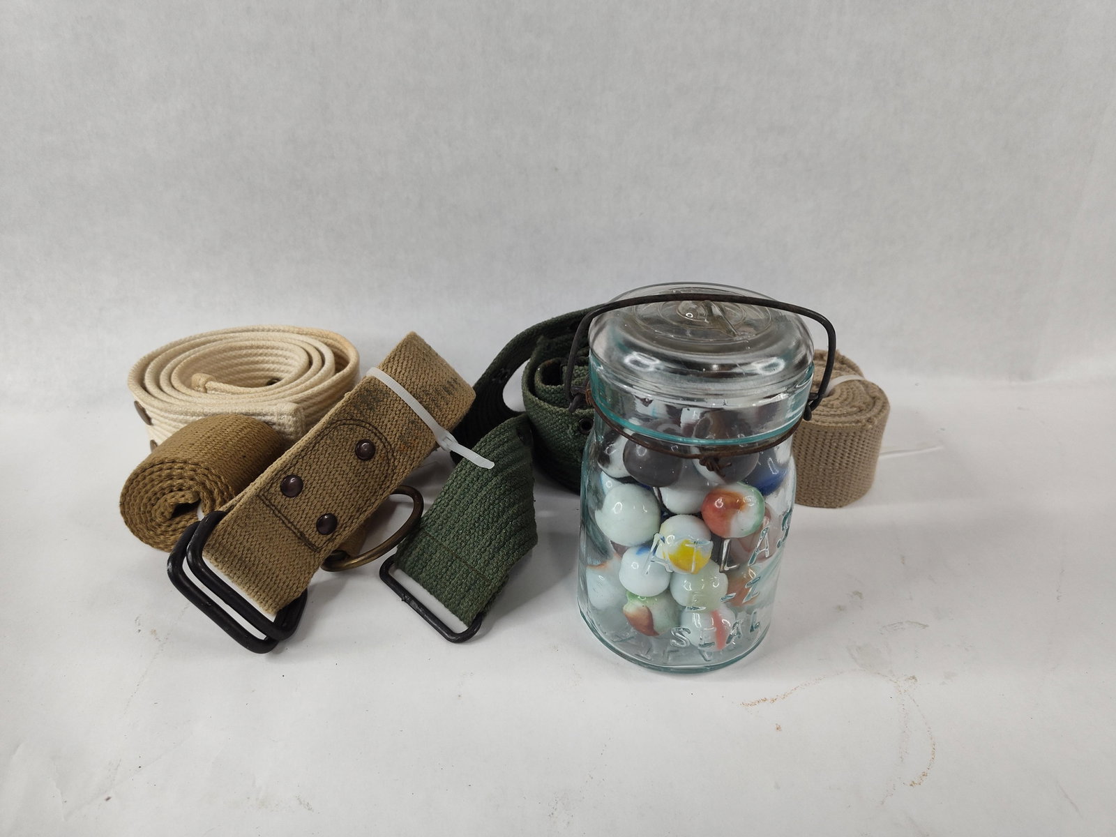 5 U.S. Military Web Belts & Atlas Jar: This lot features five U.S. military-style web belts and an antique glass canning jar containing approximately 40 to 50 marbles. The military equipment includes one white cotton web belt for ceremonia