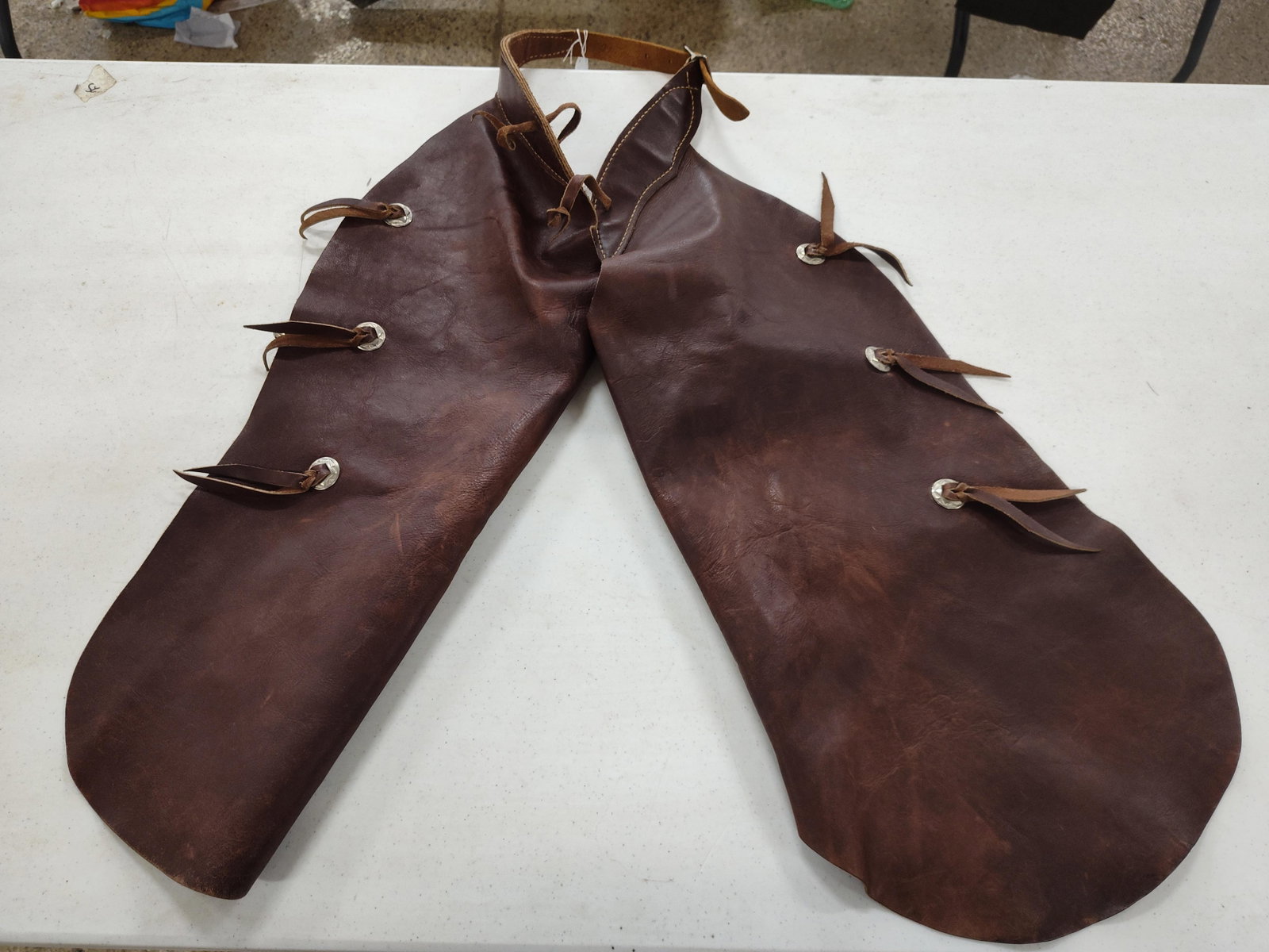 Pair Western Brown Leather Star Chinks: A pair of Western leather chinks crafted from heavy-grade brown oil-tanned leather with a roughout suede interior. The garment features a two-piece design joined by an adjustable waist belt. Each leg
