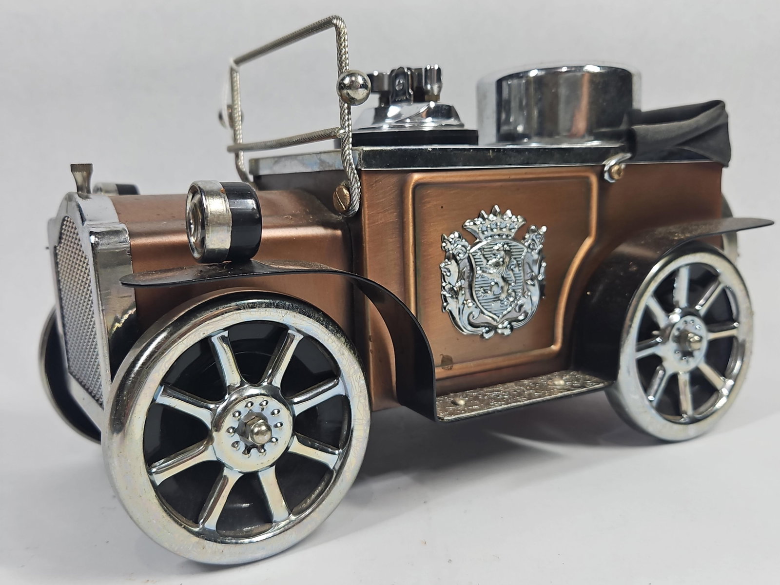 Japanese Smoking Set: A Japanese novelty smoking set modeled as an early 20th-century touring car, featuring a copper-toned metal body with chrome-plated accents. The vehicle is designed with a red-lined interior deck cont