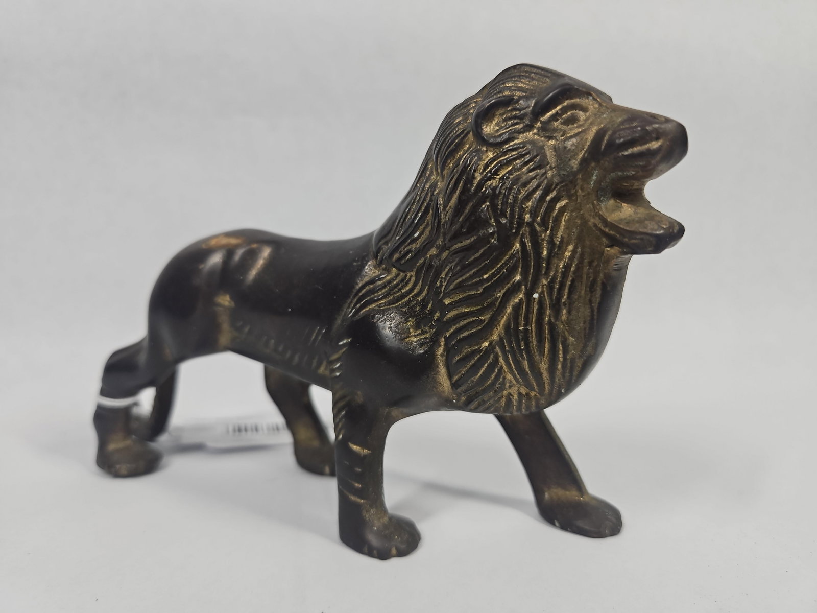 Vtg Cast Metal Roaring Lion Figurine: A cast metal figurine of a roaring lion depicted in a standing posture. The piece features a stylized mane with deep linear texturing and decorative horizontal ribbing on the front legs. It is