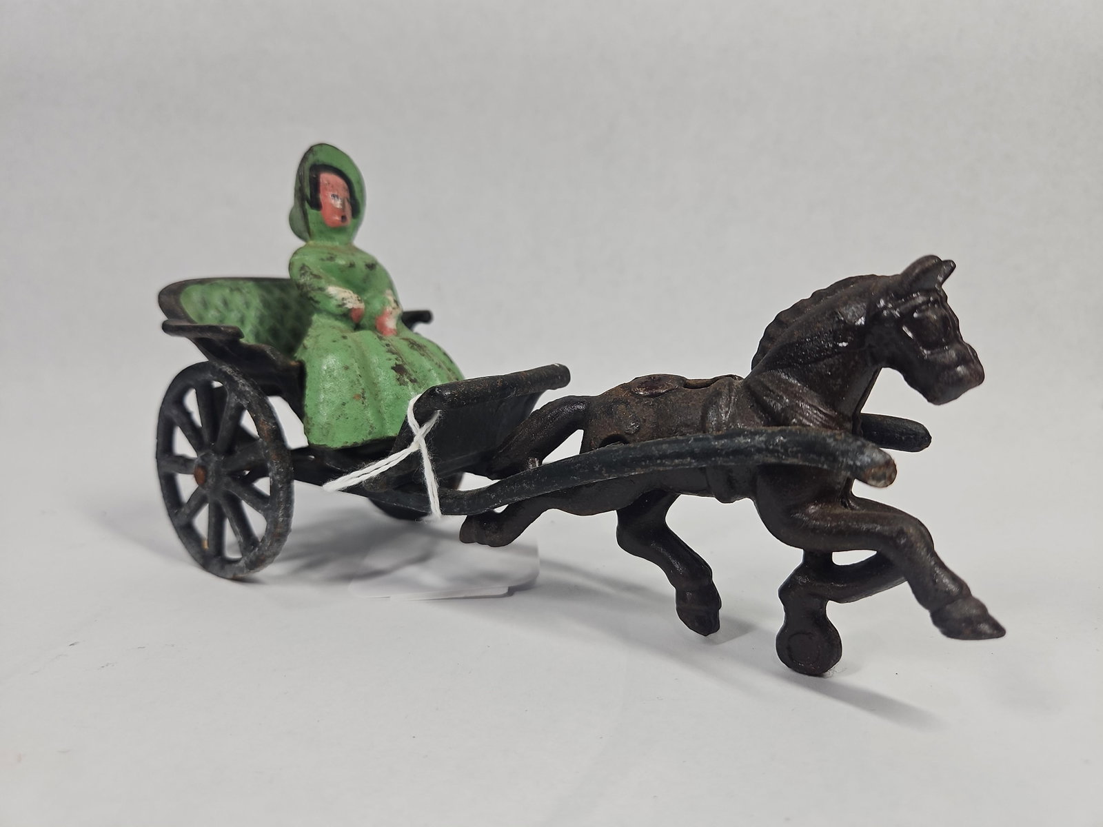 Galloping Horse Carriage w/ Passenger: This cast iron toy depicts a single horse-drawn carriage or buggy. The set includes a single horse cast in a galloping pose with a dark brown or black finish. The horse is connected by two shafts to a