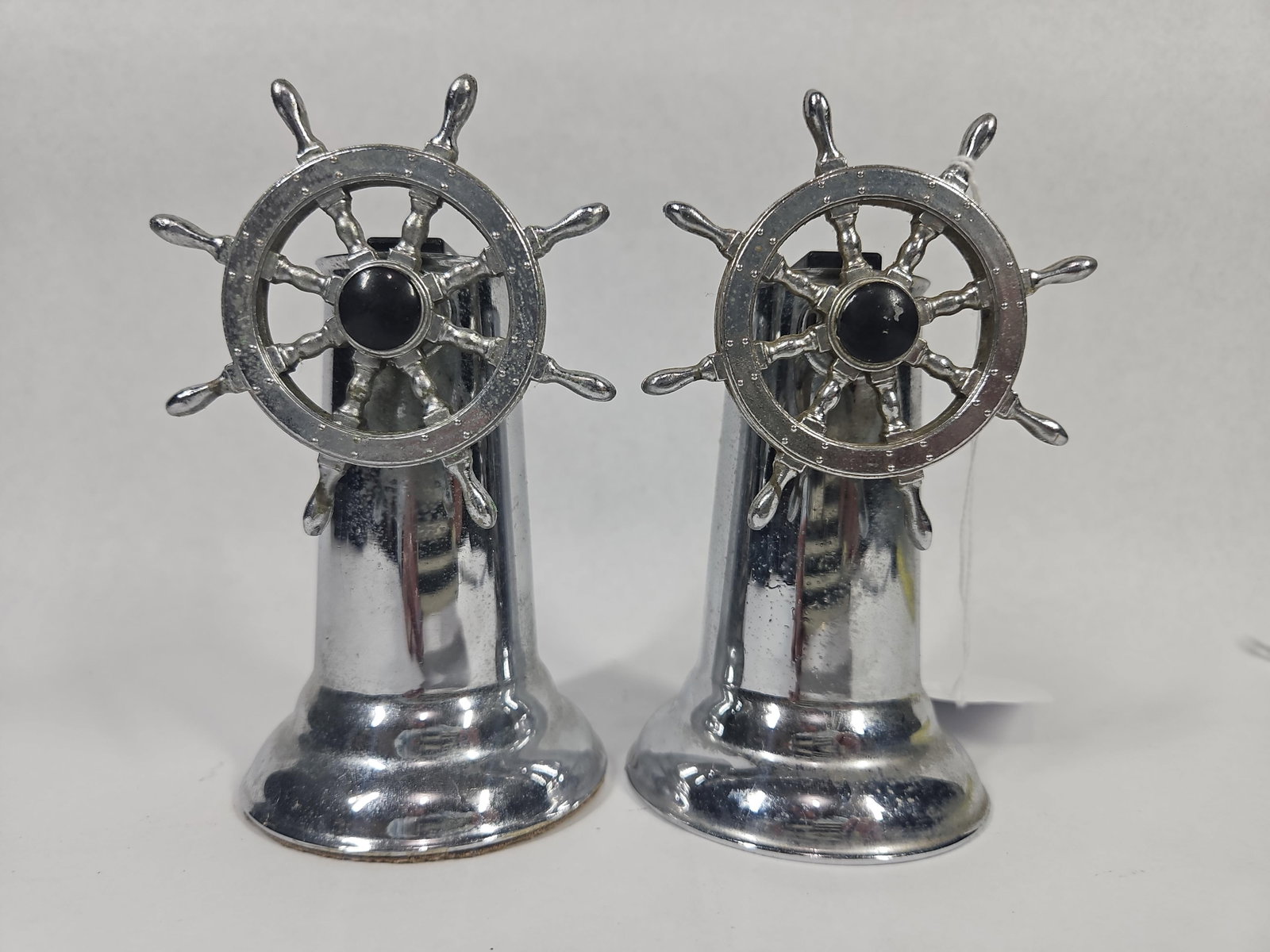 Pair American Ship Wheel Table Lighters: A pair of vintage chrome-plated table lighters featuring a nautical ship steering wheel motif. Each piece consists of a tapered, flared pedestal base with a miniature steering wheel mounted to the sid
