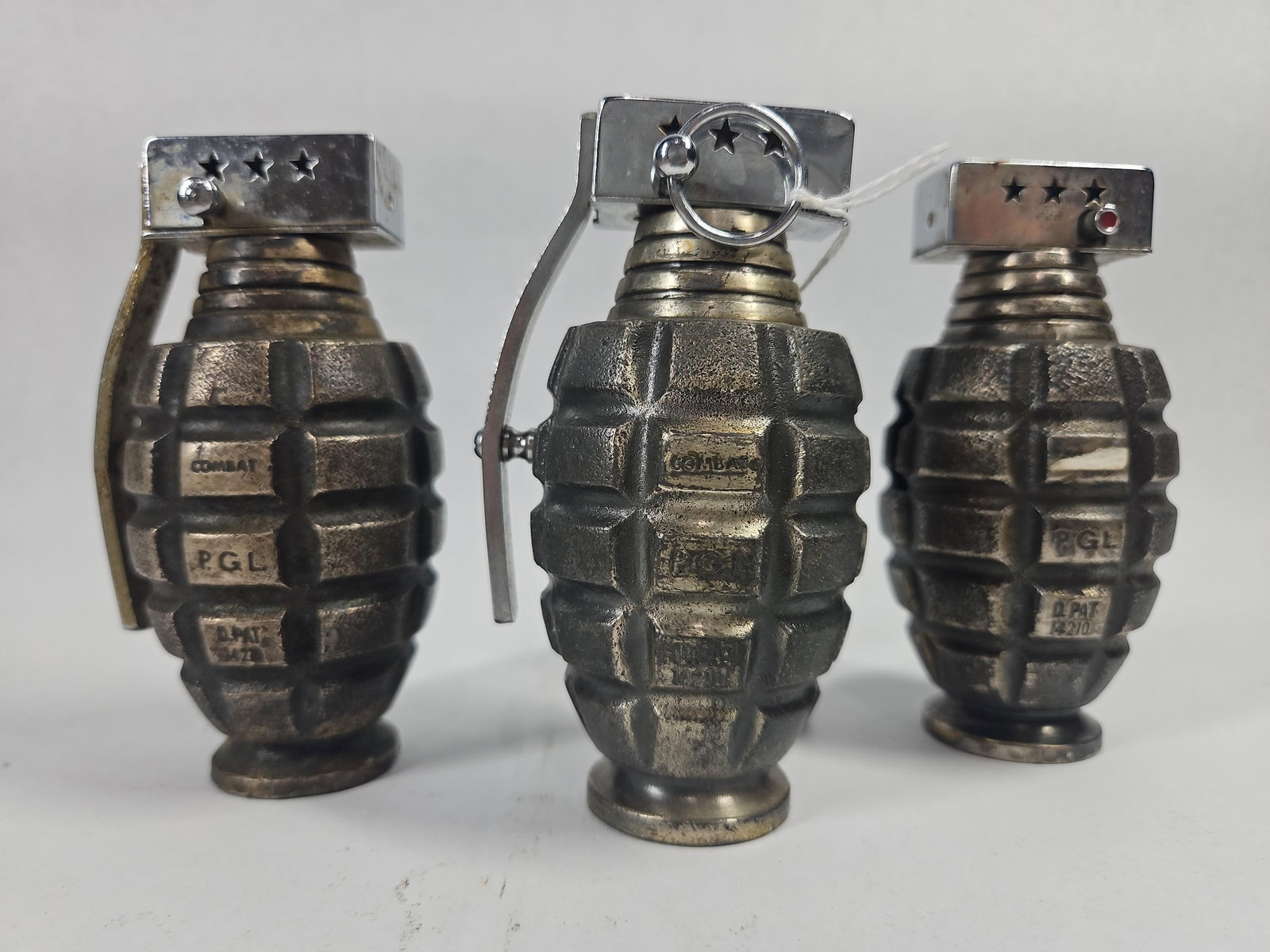 3 P.G.L. Hand Grenade Table Lighters: This lot consists of three table lighters designed in the form of MK2 pineapple style hand grenades. The bodies are constructed of heavy cast metal with a textured fragmentation pattern and a weathere