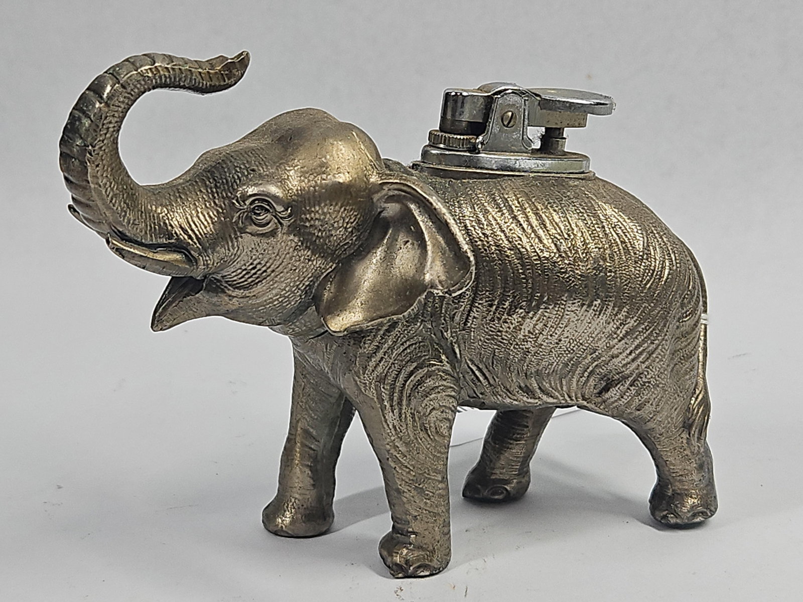 Vtg Cast Metal Elephant Table Lighter: This figural table lighter is constructed from cast metal in the form of a standing elephant with a raised trunk and an open mouth. The body of the figure features a heavily textured surface designed