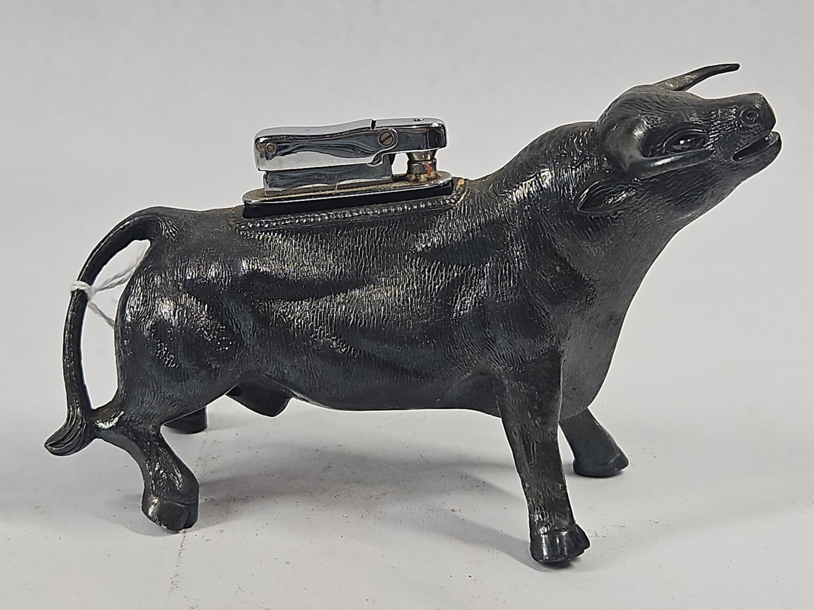 Vtg Cast Metal Bull Table Lighter: This vintage table lighter is designed as a cast metal figurine of a bull in a bellowing pose with its head upturned and horns swept back. The figurine features a black-toned, textured finish