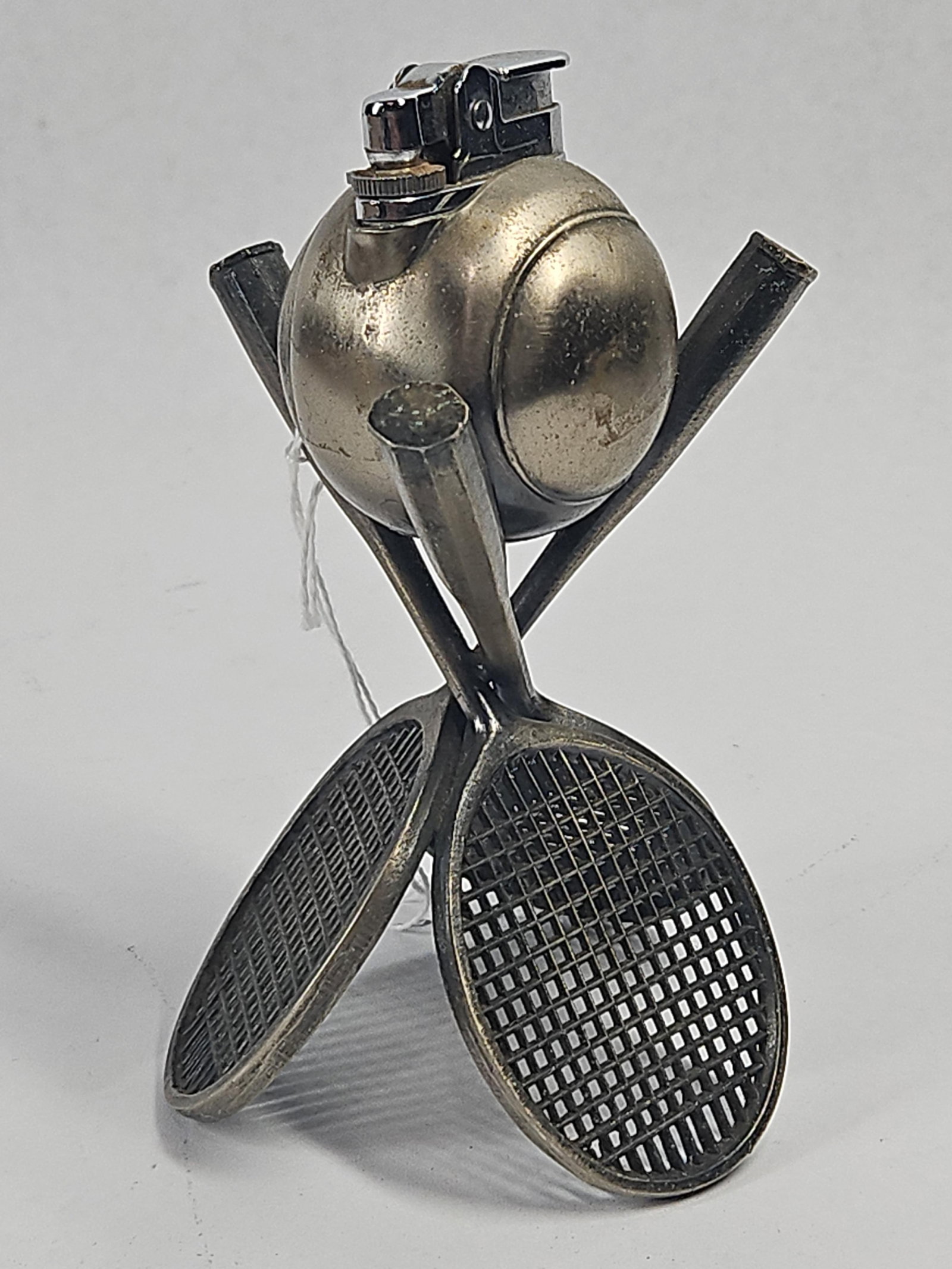 Vtg Cast Metal 3-Racket Tennis Lighter: A vintage cast metal novelty table lighter in a tennis theme. The base consists of three stylized tennis rackets with open-grid stringing patterns, crossed at the handles to form a tripod support. A