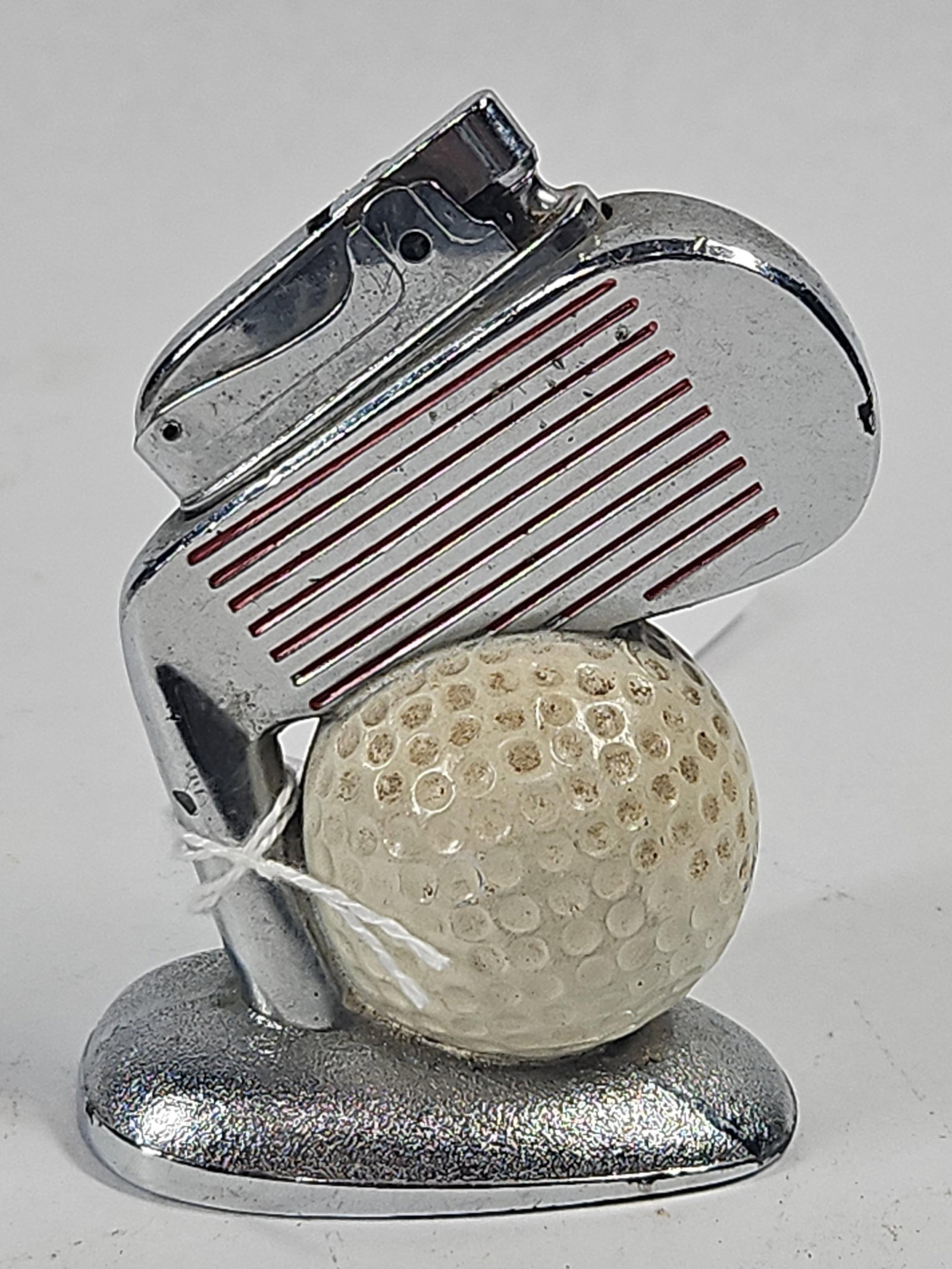 Japanese Golf Club & Ball Table Lighter: A Japanese chrome-plated metal novelty table lighter designed with a golf theme. The piece features a stylized golf iron head positioned as if striking a dimpled golf ball. The face of the club head