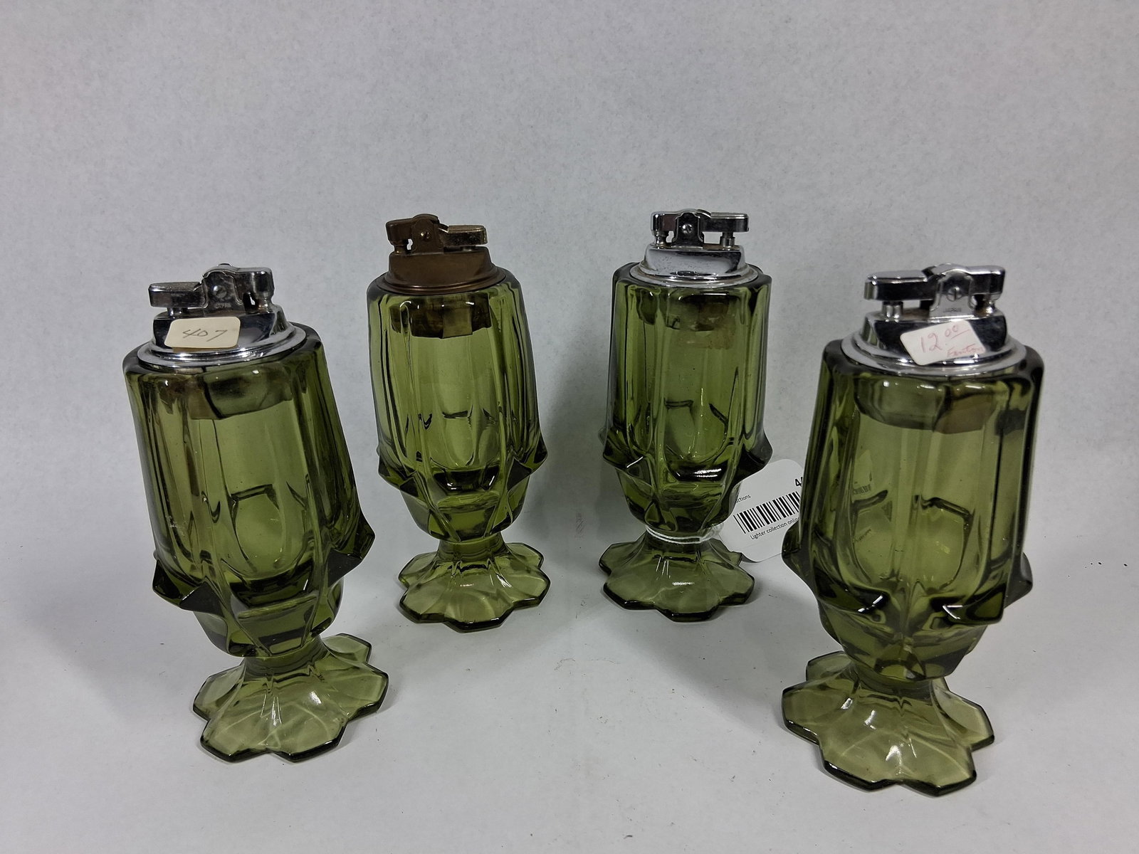 Set Fenton Green Pressed Glass Lighters: A collection of Japanese table lighters featuring olive green pressed glass bases and removable metal lighter mechanisms. The glass components are designed in the Valencia pattern with faceted, panele