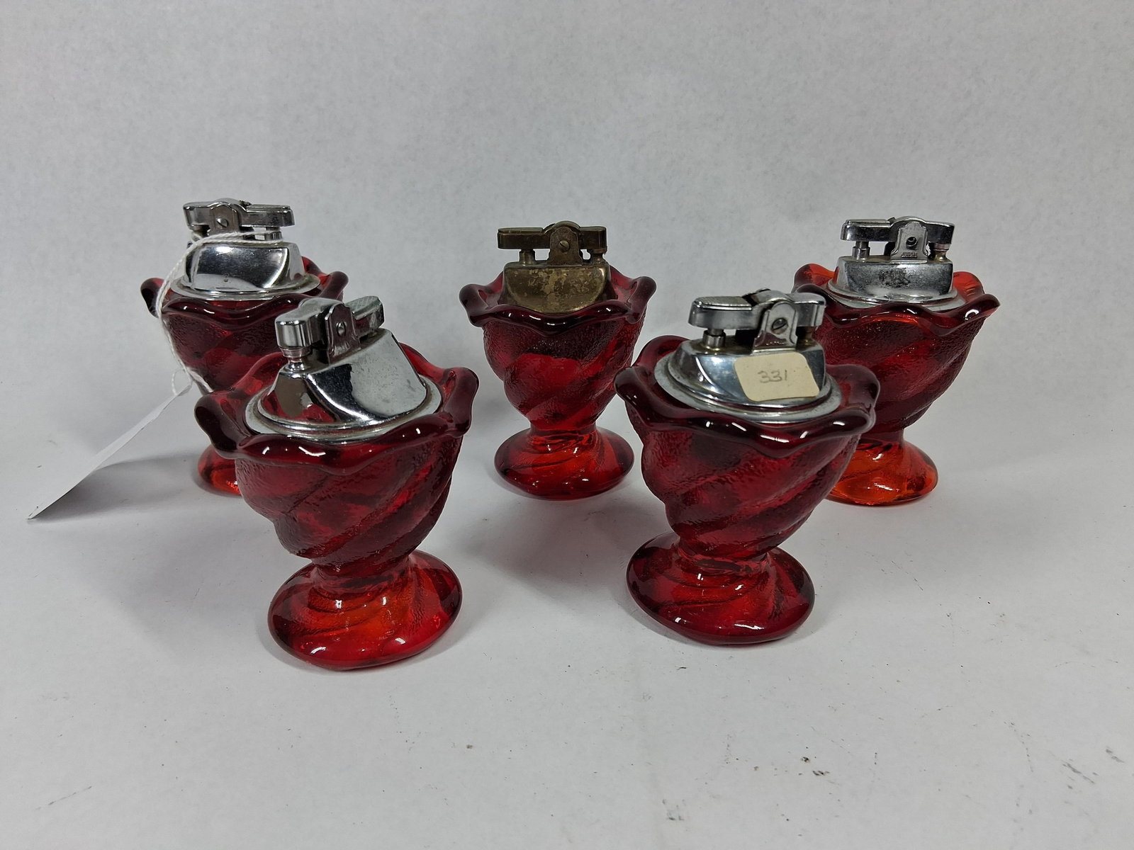Set 5 Japanese Amberina Table Lighters: This set of five table lighters features decorative pedestal bases crafted from translucent ruby-red glass. The glass is molded with a distinct swirl pattern, transitioning into ruffled, petal-style
