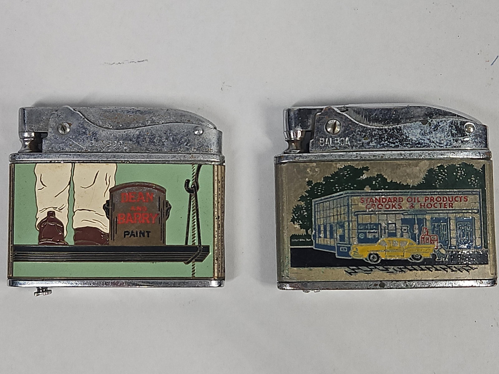 Pair Balboa & Dundee Japanese Lighters: This lot consists of two Japanese chrome-plated pocket lighters featuring regional lithographed advertising for Columbus, Ohio-based businesses. The first lighter, manufactured for the Sohio