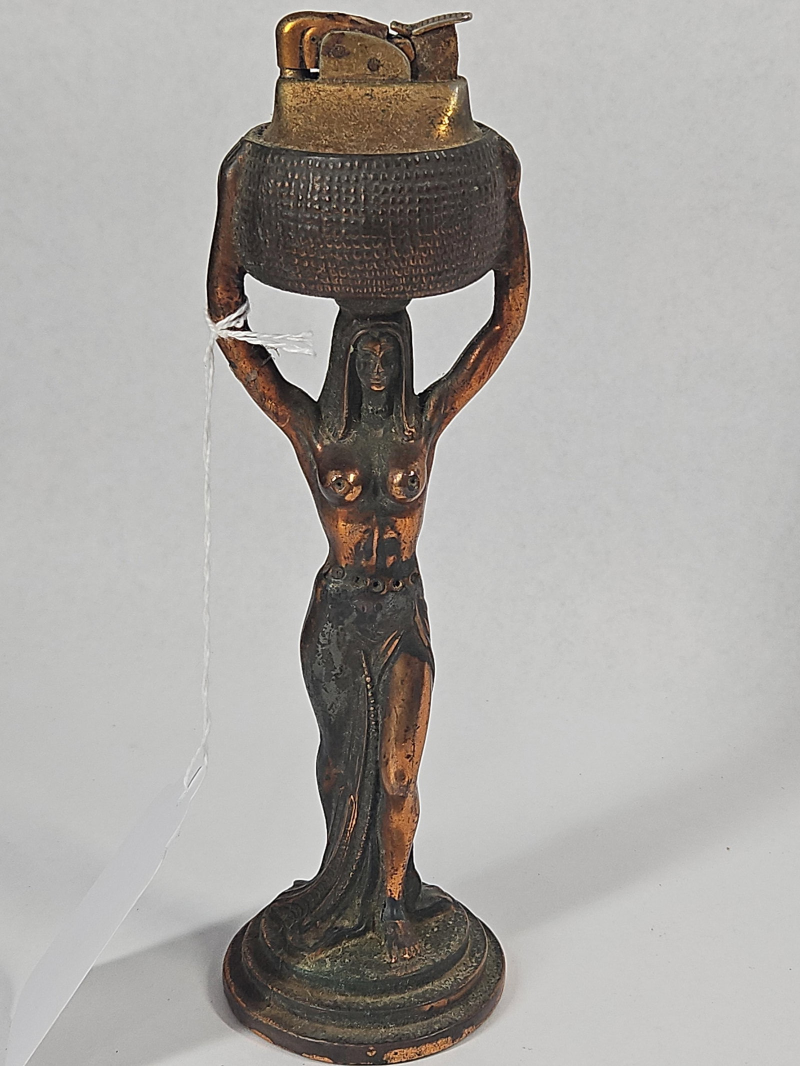 Egyptian Revival Figural Table Lighter: A vintage Egyptian Revival style figural table lighter featuring a cast metal base in the form of a woman carrying a textured basket on her head. The figure is depicted in a stylized Art Deco manner,