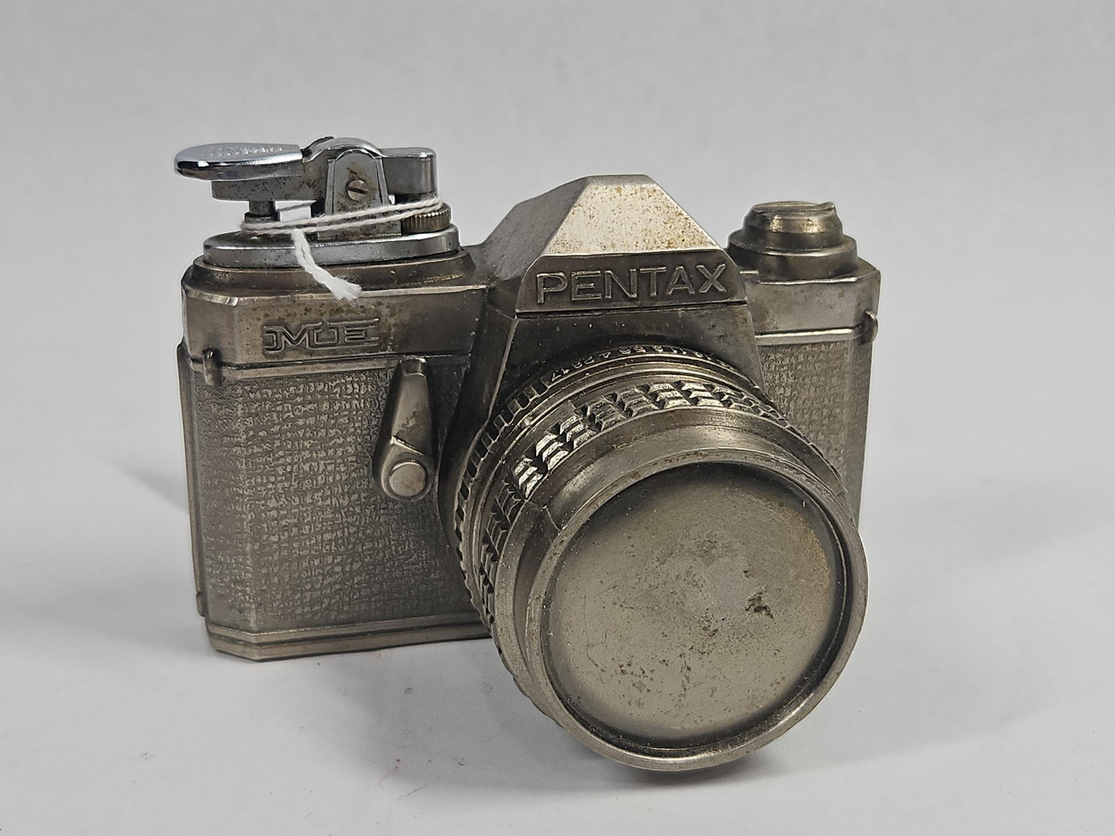 Japanese Pentax ME Camera Table Lighter: A Japanese cast metal novelty table lighter fashioned as a miniature replica of a Pentax ME SLR camera. The body features a textured silver-tone finish intended to mimic camera leatherette, mounted