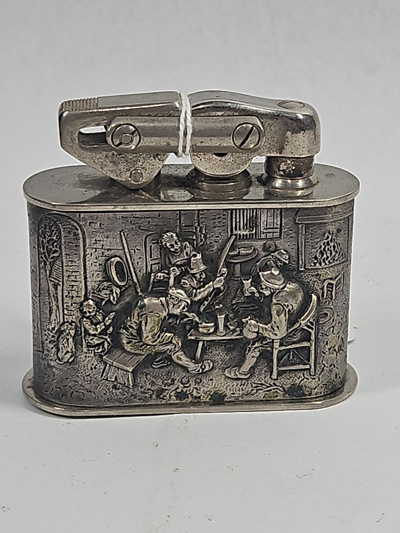 Vtg Lift-Arm Tavern Table Lighter: A vintage petrol table lighter featuring a lift-arm mechanism and a silver-toned metal body. The exterior is decorated with high-relief cast tavern scenes on both major faces, depicting figures in