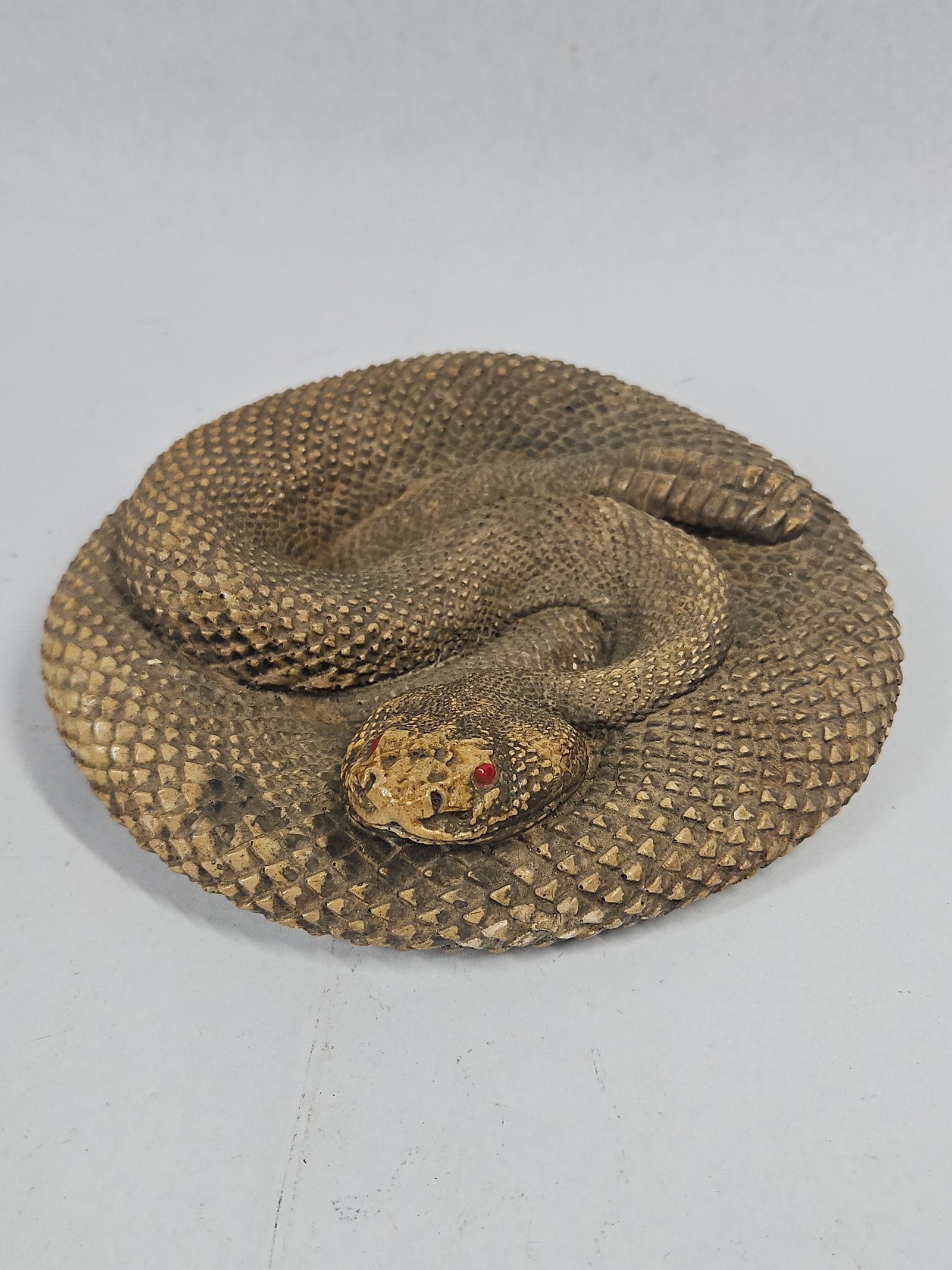 A Coiled Rattlesnake Chalkware Figurine: A cast plaster or chalkware figurine of a coiled rattlesnake. The snake is modeled in a circular, resting position with its head slightly elevated and its segmented rattle tucked into the interior