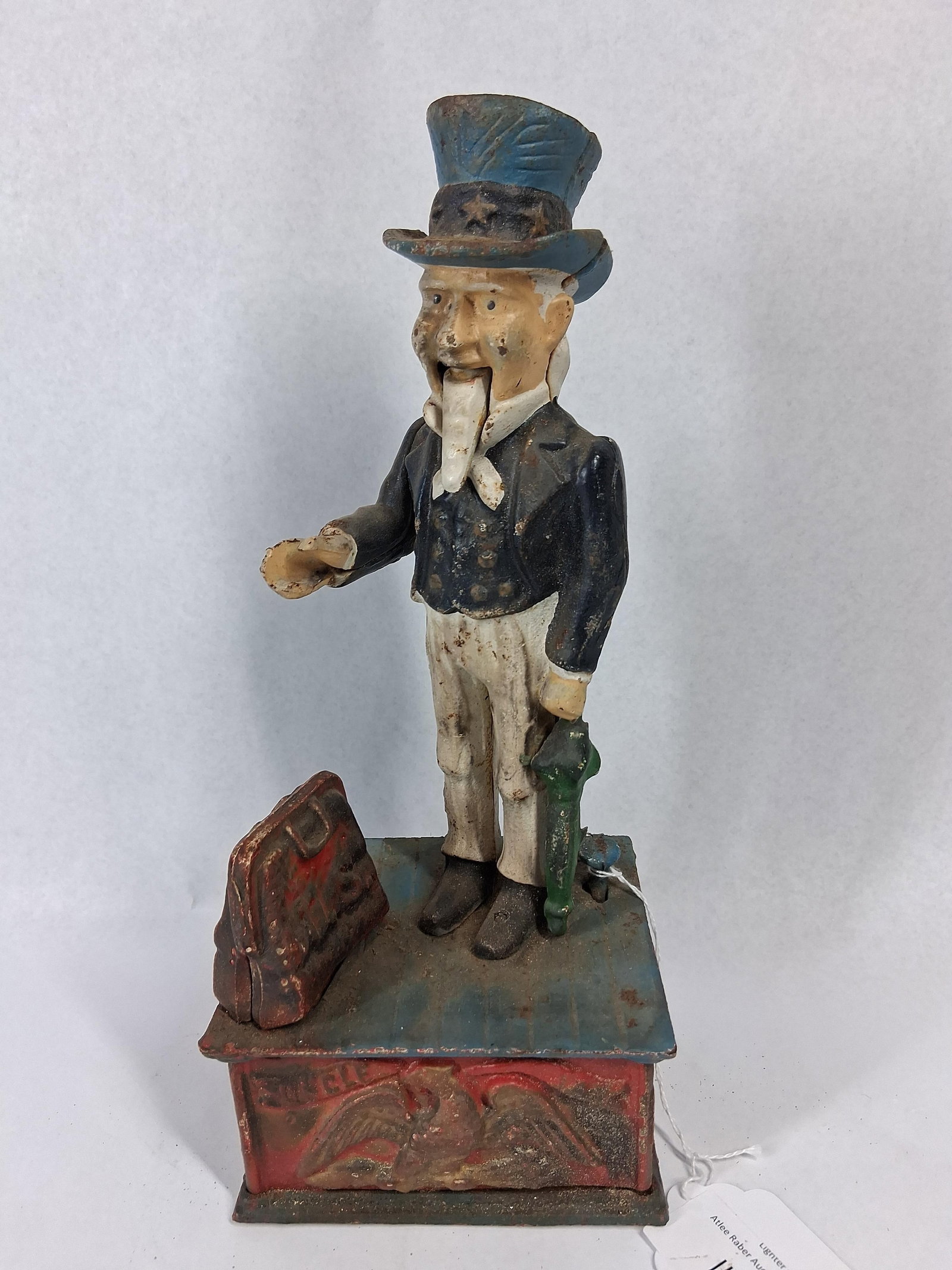 Cast Iron Uncle Sam Mechanical Bank: This mechanical bank is constructed of painted cast iron and features the figure of Uncle Sam. The figure is depicted standing on a rectangular base, wearing a blue top hat decorated with stars, a