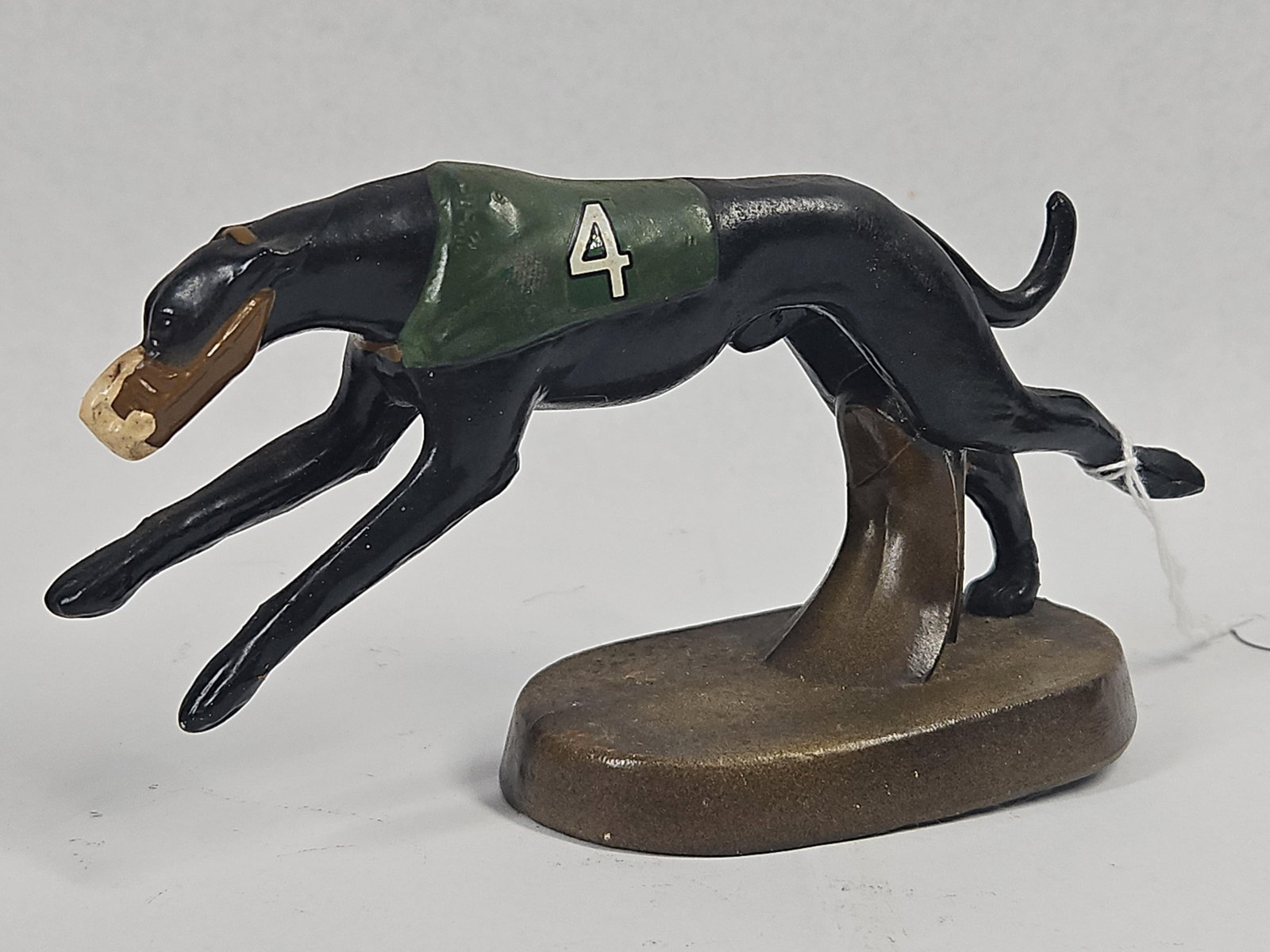Scotti-D Inc. Greyhound Bottle Opener: A cast metal figurine of a racing greyhound that doubles as a functional bottle opener. The dog is depicted in a full running stride and is painted black, wearing a brown muzzle and a green racing
