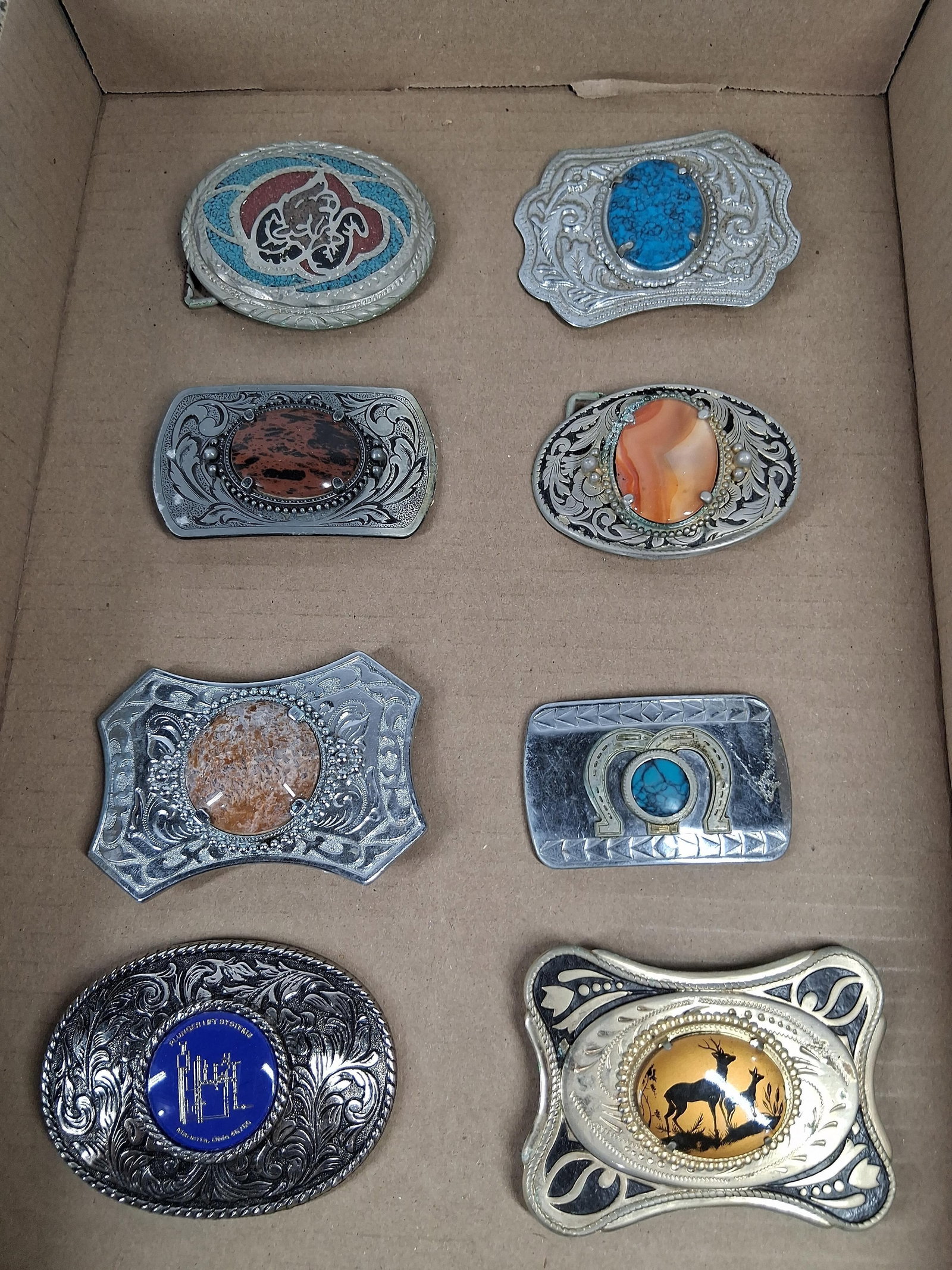 Set 8 Vtg Western Style Belt Buckles: A collection of eight vintage Western-style belt buckles featuring diverse motifs and stone-style inlays. The assortment includes a large oval silver-tone buckle with floral scrollwork borders and a