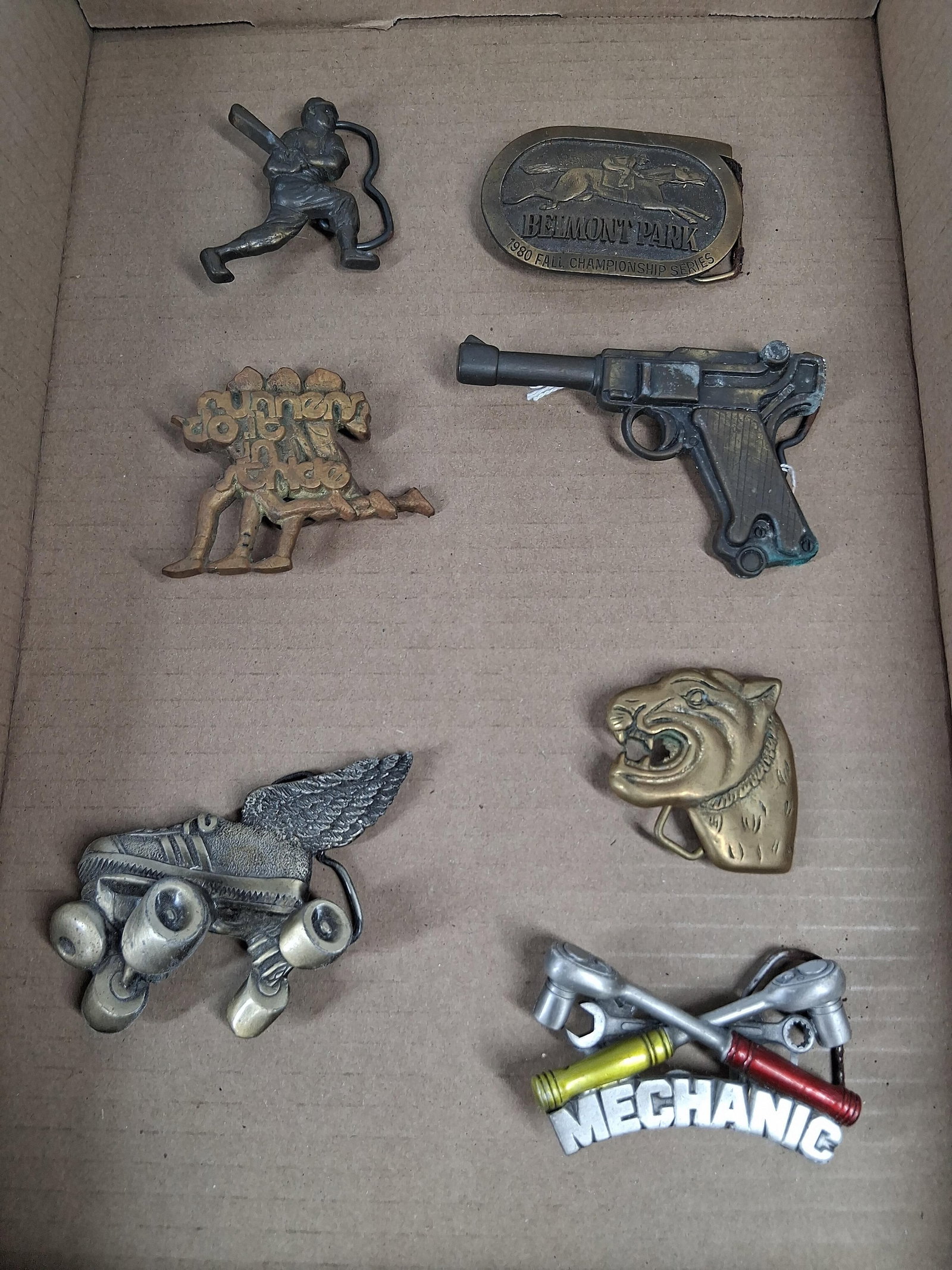 Set 7 Vtg Novelty & Commem Belt Buckles: A collection of seven vintage novelty and commemorative belt buckles in various cast metals and themes. An oval brass-toned commemorative buckle for the 1980 Fall Championship Series at Belmont Park