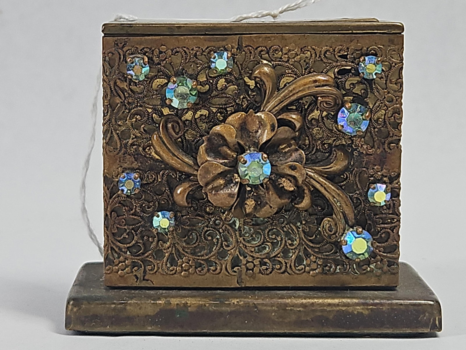 Light-O-Matic Aurora Rhinestone Lighter: This rectangular brass table lighter is constructed with a stepped base and decorative panels. All four vertical faces feature intricate scrolled brass filigree. The front and back panels are adorned 