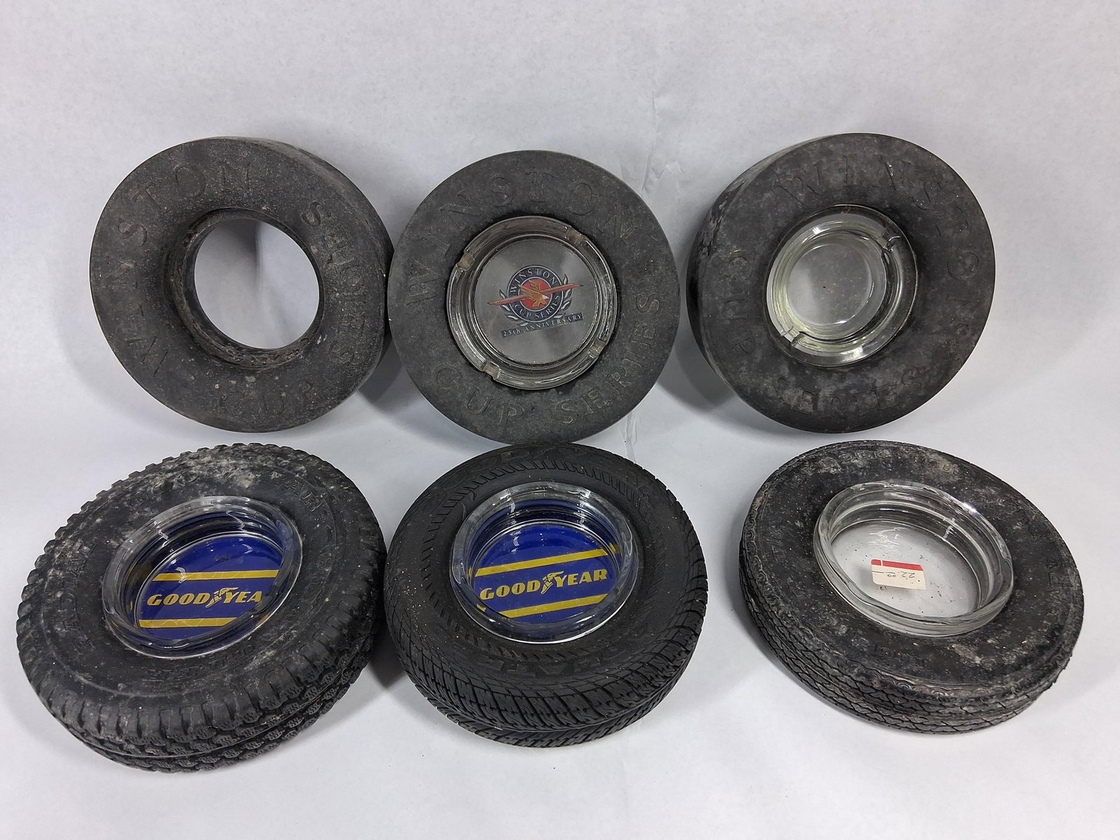 Set 6 Vtg Goodyear Rubber Tire Ashtrays: A collection of six vintage promotional ashtrays manufactured from black rubber tires with glass inserts. Three units are styled as racing slicks with embossed lettering on the sidewalls reading