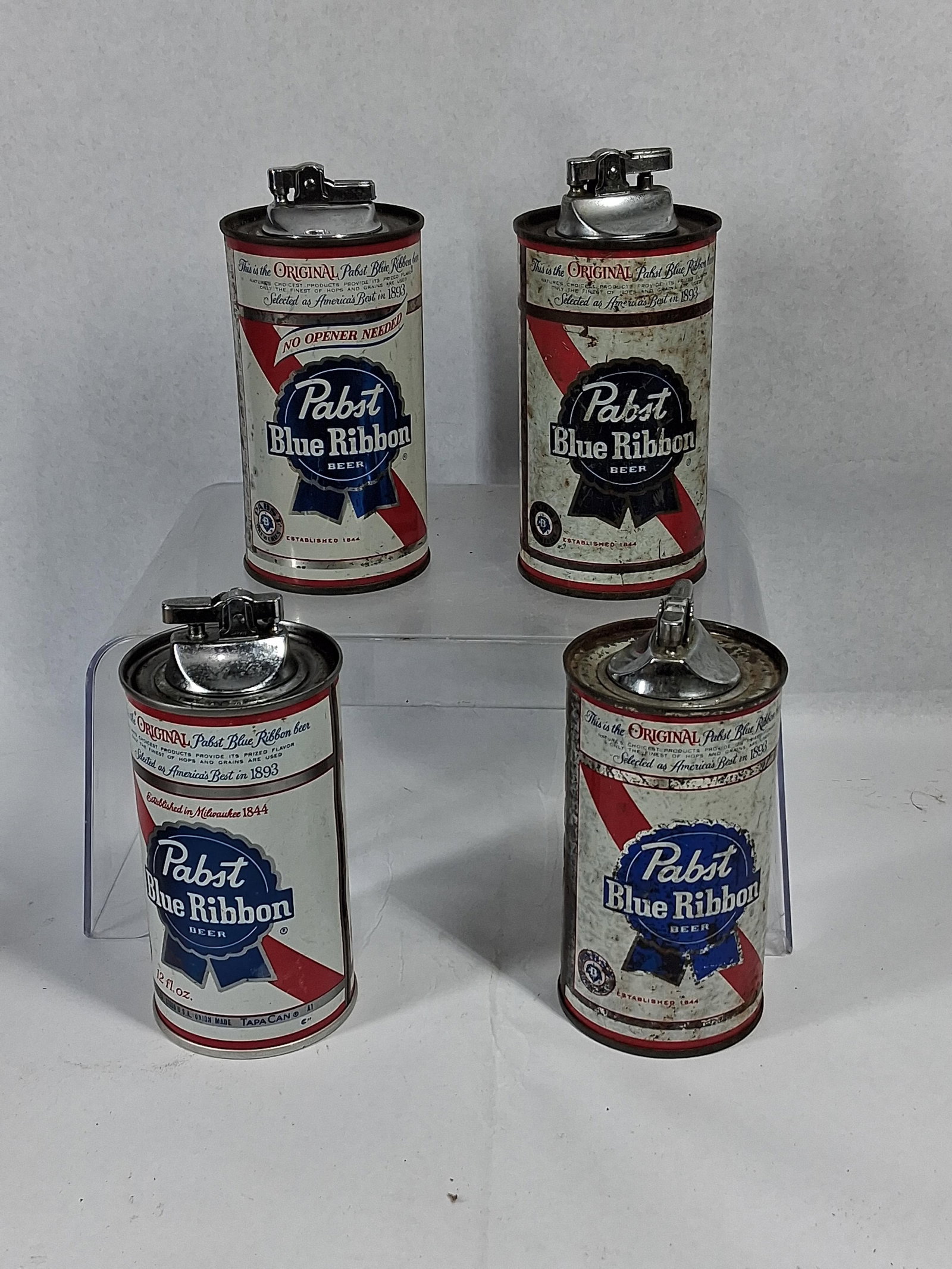 4 Pabst Blue Ribbon Beer Can Lighters: A Japanese set of four table lighters constructed from lithographed sheet metal cans for Pabst Blue Ribbon Beer. Each unit is modeled after a 12 fl. oz. flat-top beer can, featuring the brand's