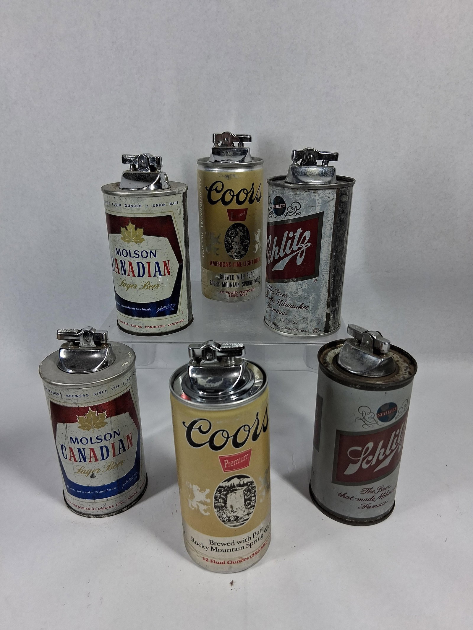 6 Vtg Molson Coors Schlitz Can Lighters: A collection of six lithographed metal table lighters designed to resemble standard 12-ounce beer cans from three major North American breweries. Each unit consists of a cylindrical body with a chrome