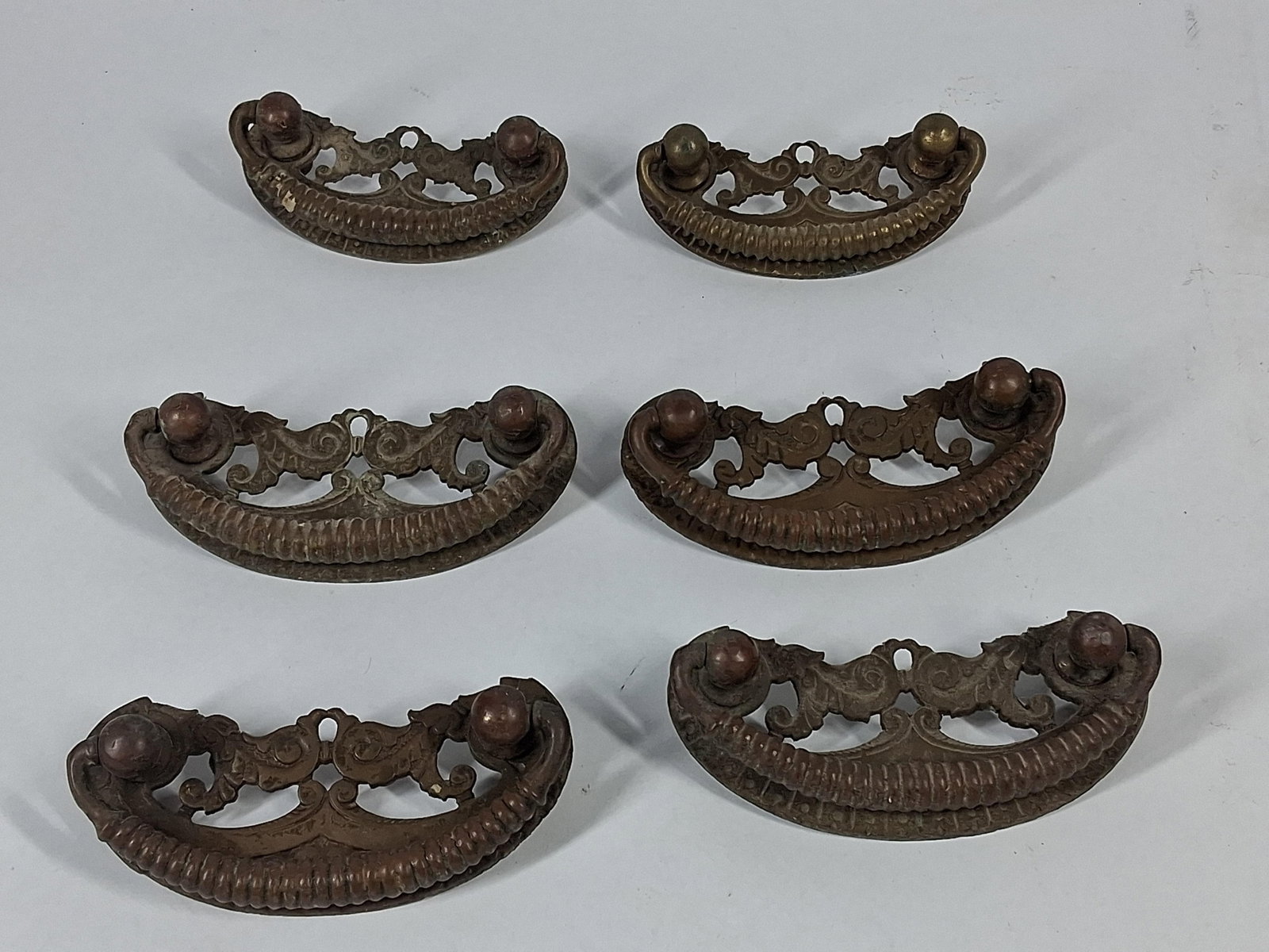 Set 6 Rococo Revival Metal Drawer Pulls: A set of six cast metal furniture drawer pulls designed in a Chippendale or Rococo Revival style. Each pull consists of a cast openwork backplate featuring symmetrical scrollwork, foliate motifs, and