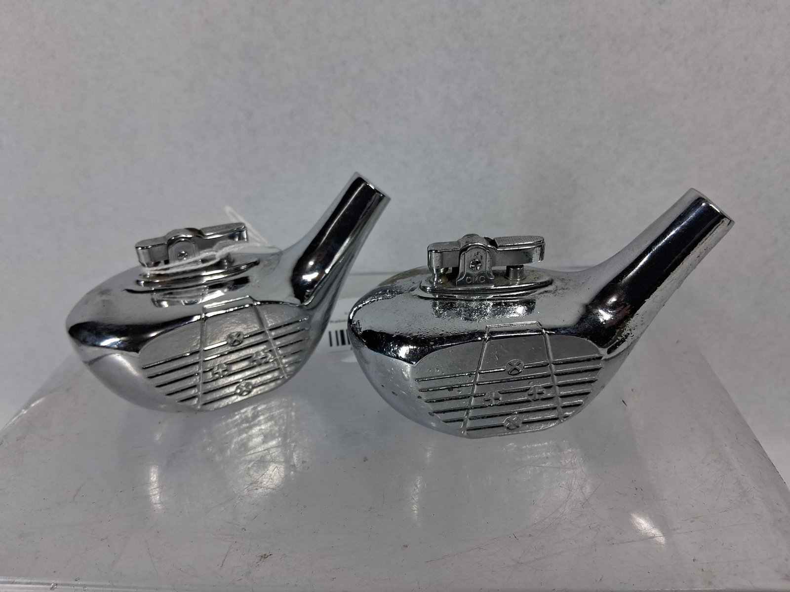 Pair GMC Chrome Golf Club Head Lighters: A pair of manual spark-ignition table lighters modeled as golf club heads, specifically drivers or woods. Each piece is constructed from cast metal with a polished chrome-plated finish. The club