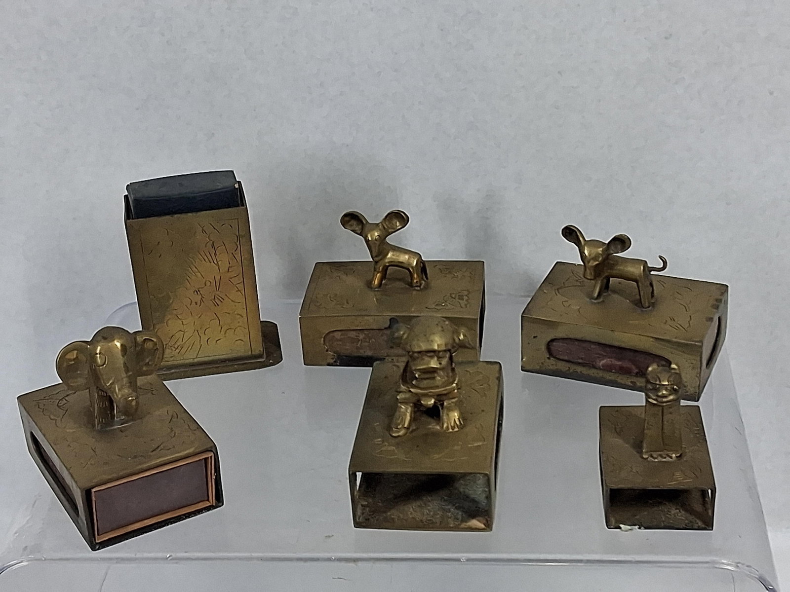 Chinese Brass Animal Matchbox & Holder: A group of brass smoking accessories including five matchbox covers and one upright holder. The pieces are constructed from cast and sheet brass with hand-incised decorative details. Each of the five 