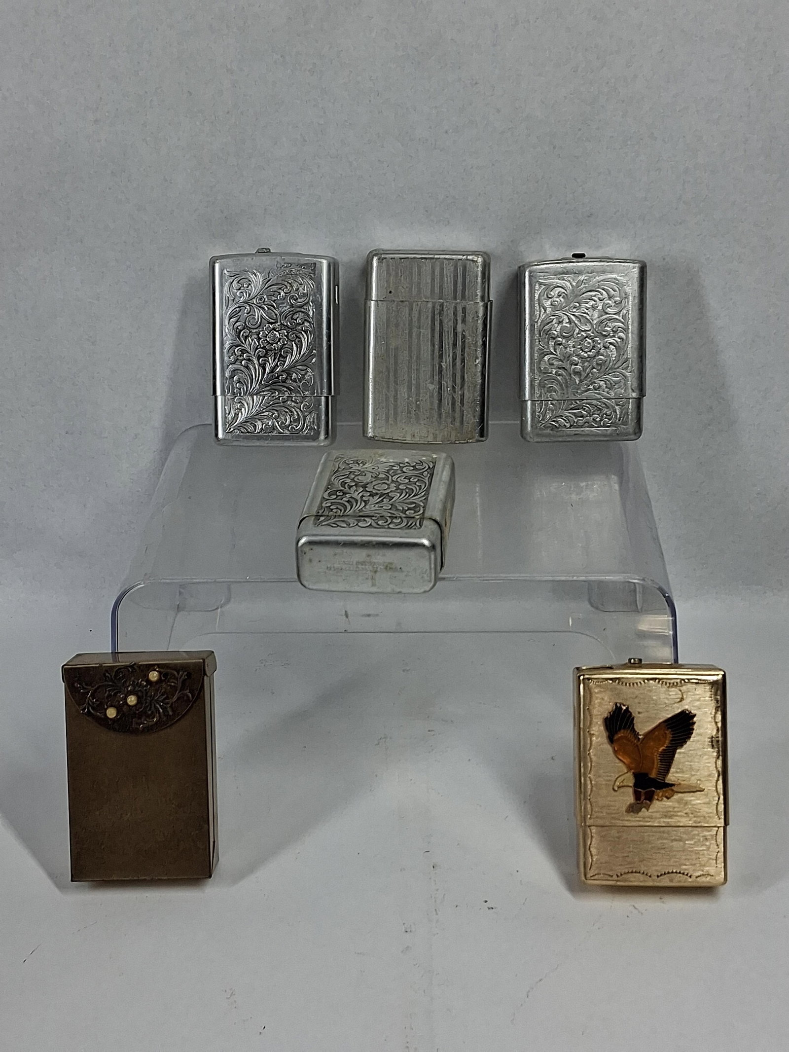 Park Industries Vtg Lighters & Cases: An assortment of vintage metal pocket lighters and cigarette cases featuring various finishes and decorative motifs. The collection includes three silver-toned cases with embossed floral and acanthus 