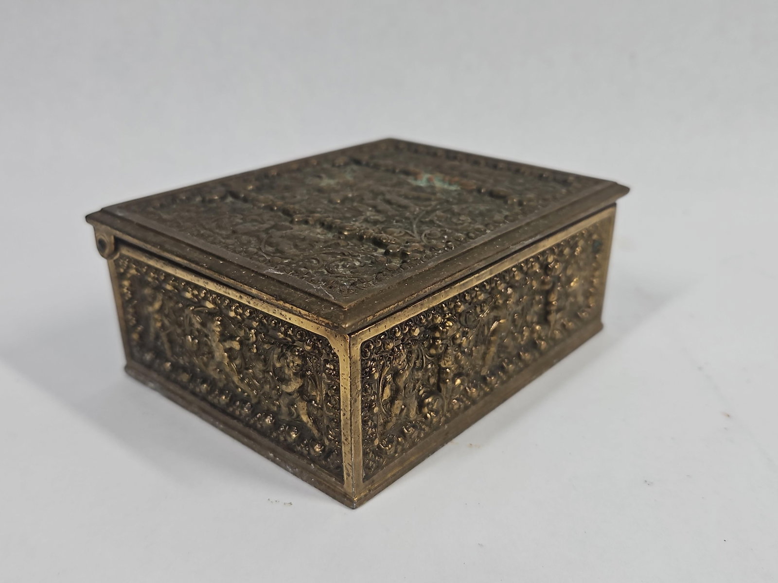 Cast Brass Wood Lined Putti Jewelry Box: This rectangular trinket box is constructed from cast brass panels joined over a wooden interior frame. The exterior surfaces are decorated with high-relief cast ornamentation in the Neoclassical styl